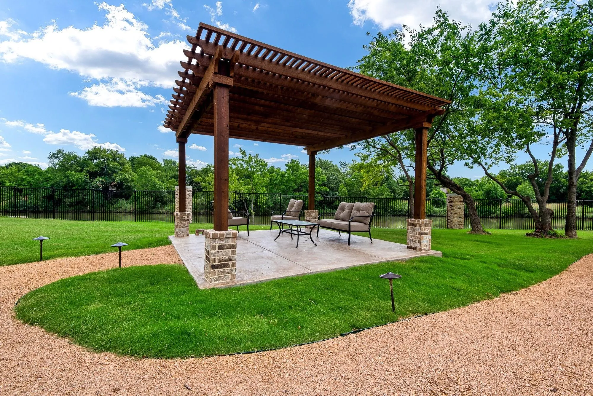Outdoor living area featuring a wooden pergola with stone-clad pillars, a paved patio, and a gravel path