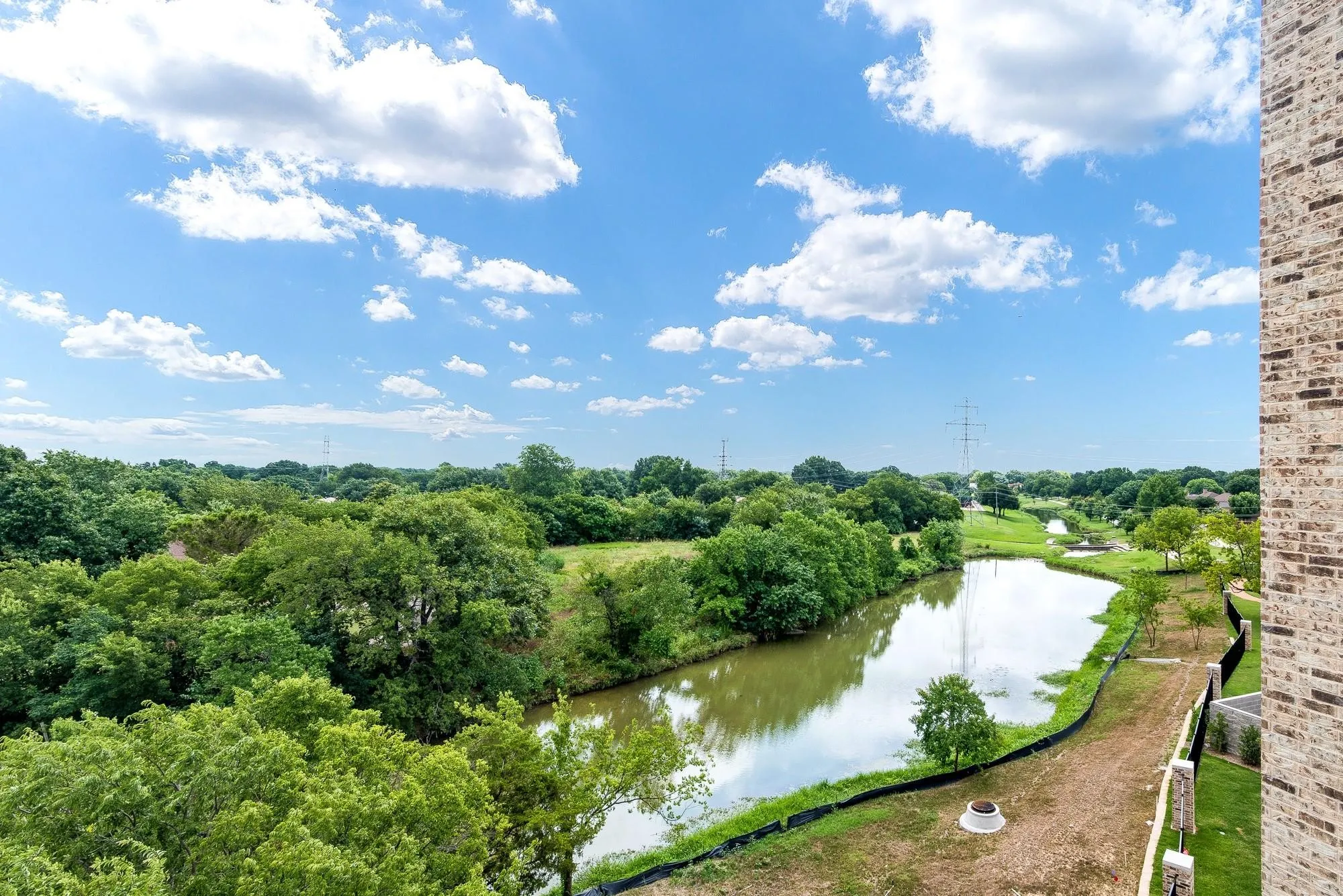 Lush green landscape with a winding body of water, offering scenic views under a bright blue sky with white clouds