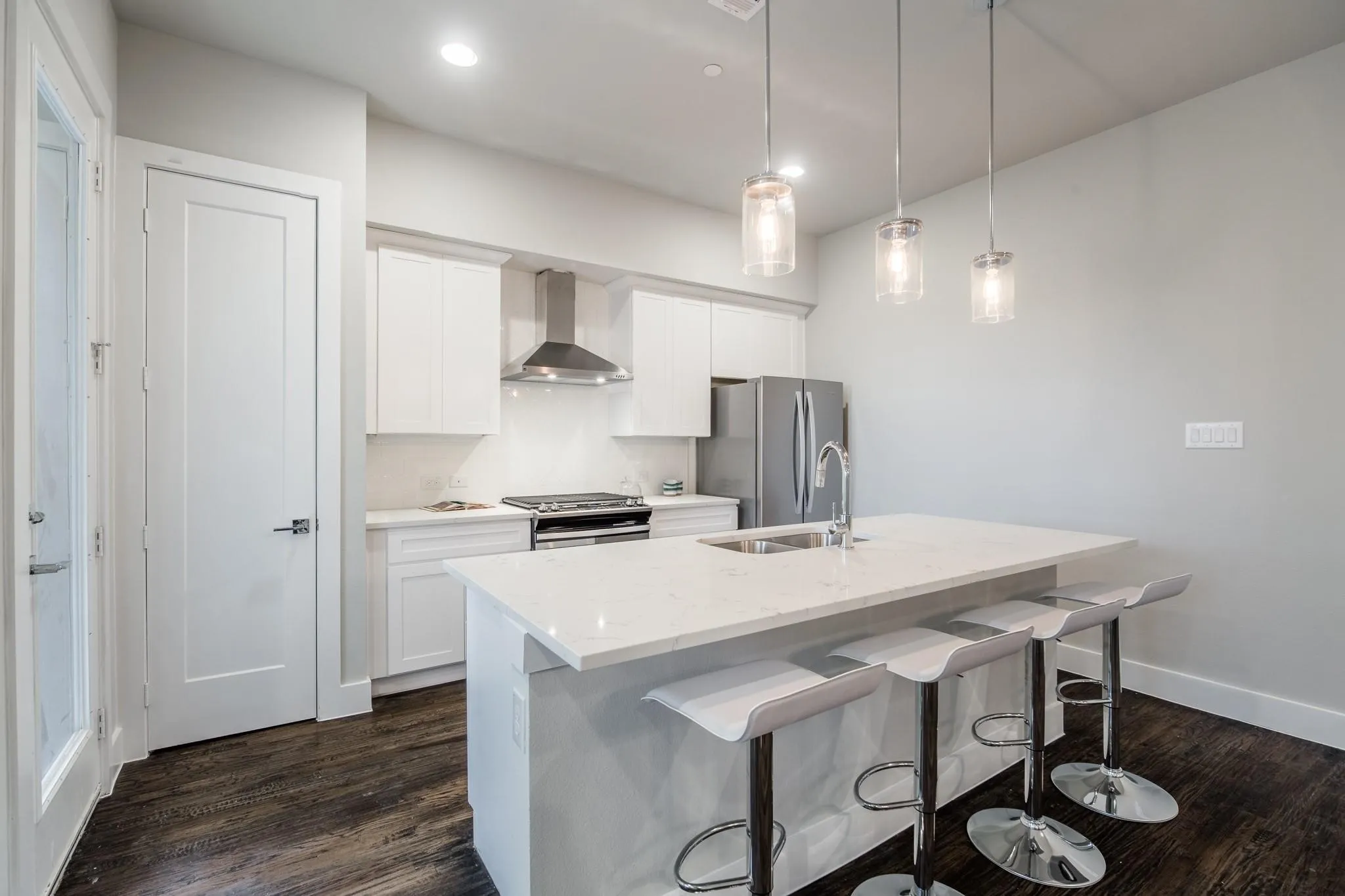 Kitchen with dark hardwood flooring, white cabinetry, a stainless steel range hood, and a kitchen island with a sink and pendant lighting