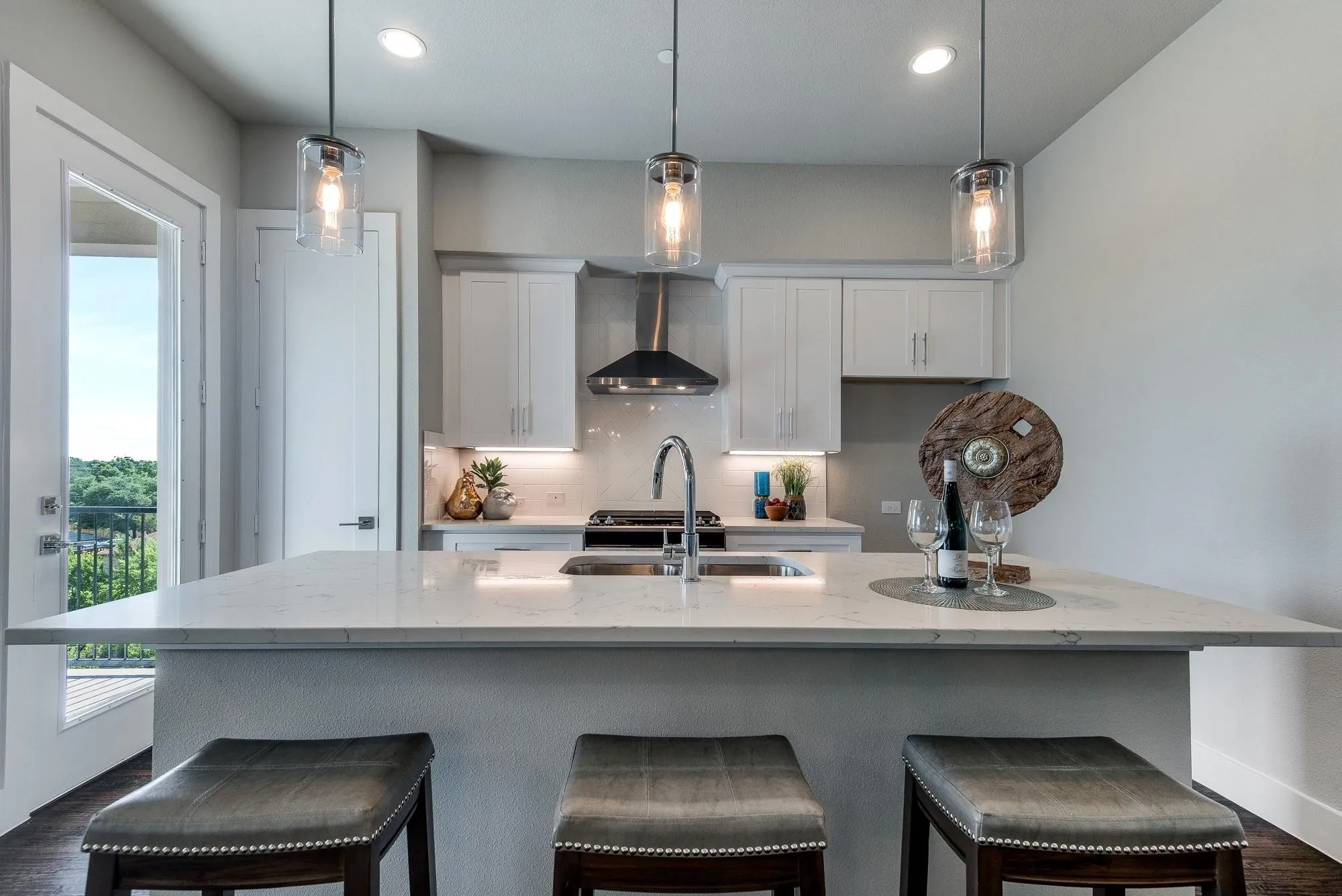 The kitchen features white cabinetry, a stainless steel range hood, an island with a sink and pendant lighting, and access to a balcony