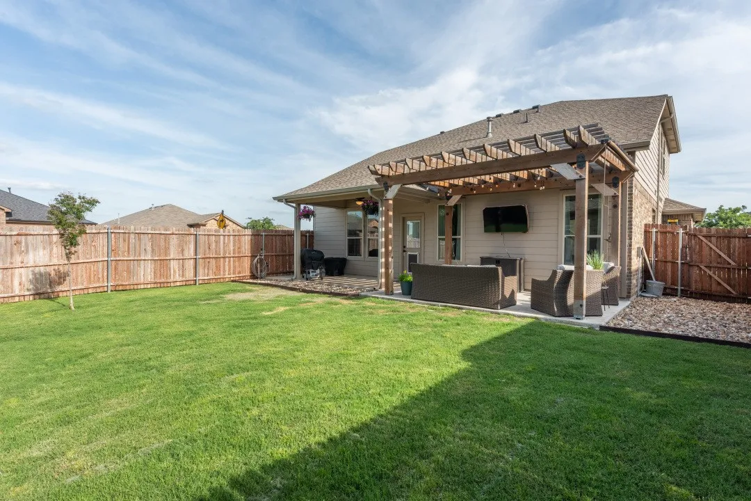Manicured backyard featuring a full privacy fence, established lawn, and a covered patio with a decorative pergola