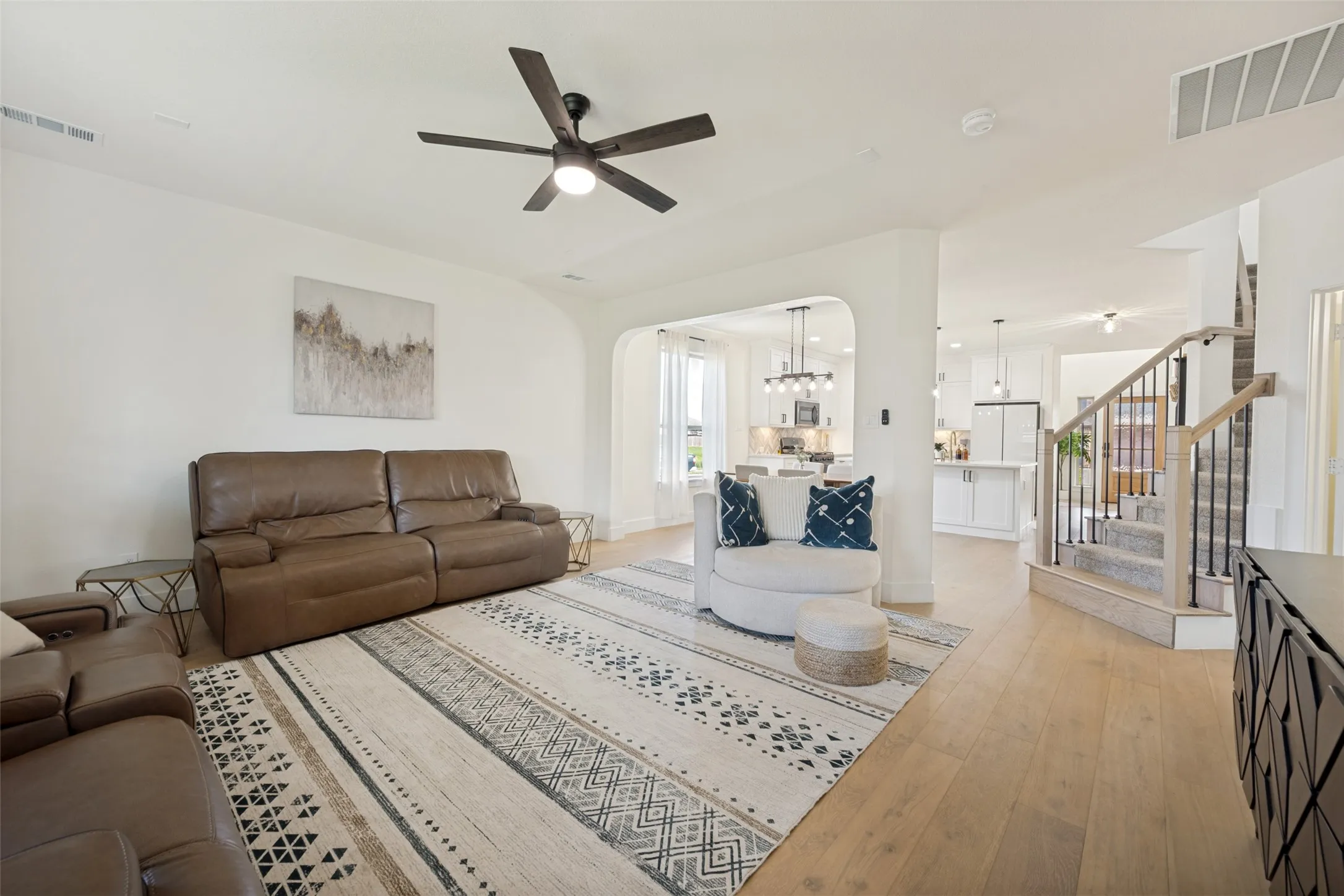 Expansive living area with light wood-finish flooring, a contemporary ceiling fan, and arched entryway