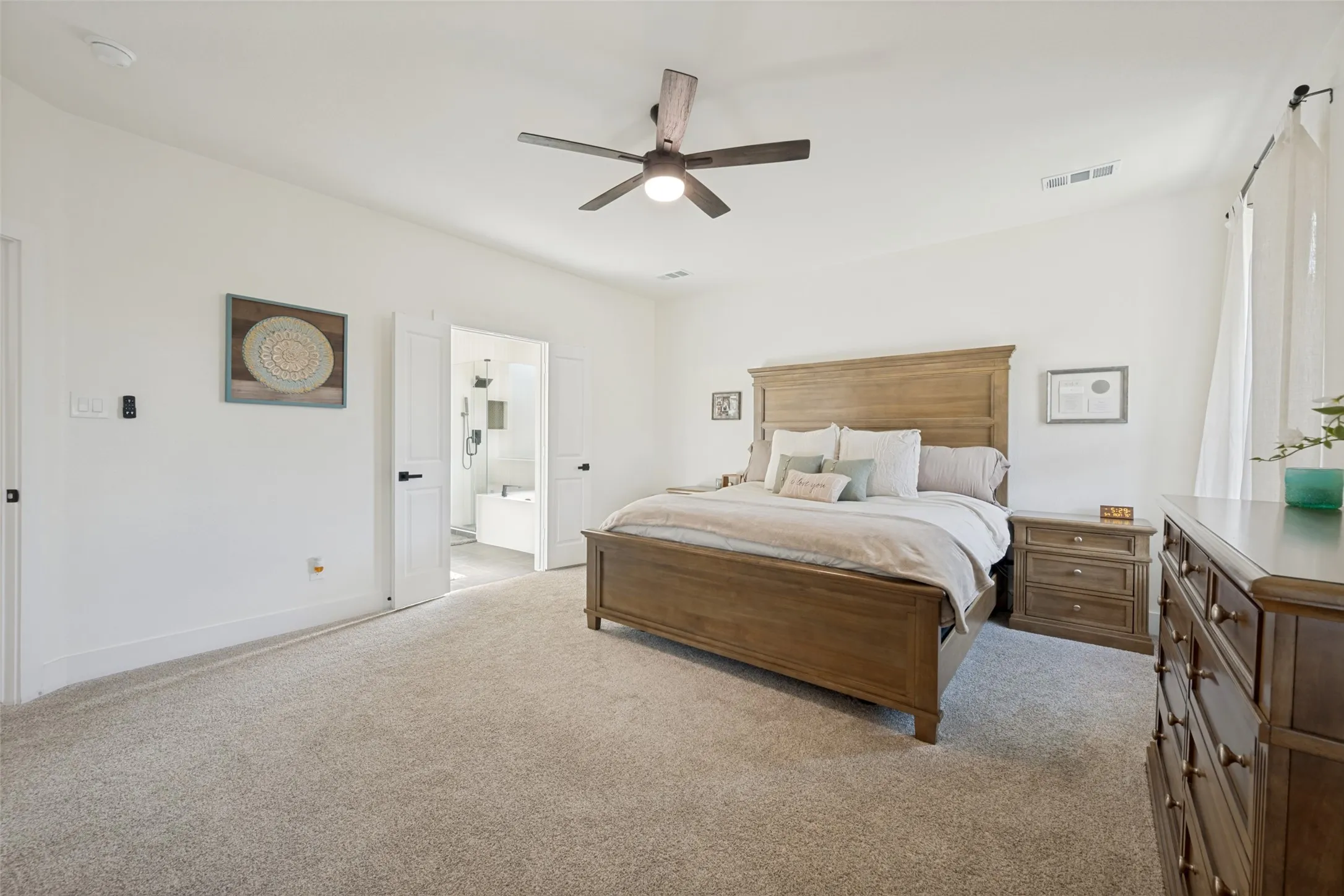 Spacious interior featuring neutral-toned carpeting, a ceiling fan with integrated lighting, and a white paneled door leading to an adjacent bathroom