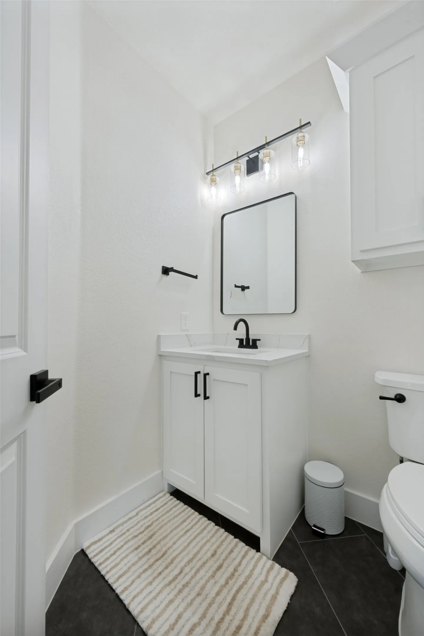 Powder room featuring a white vanity with quartz-finish countertop, black hardware, a rectangular mirror, and dark tile flooring