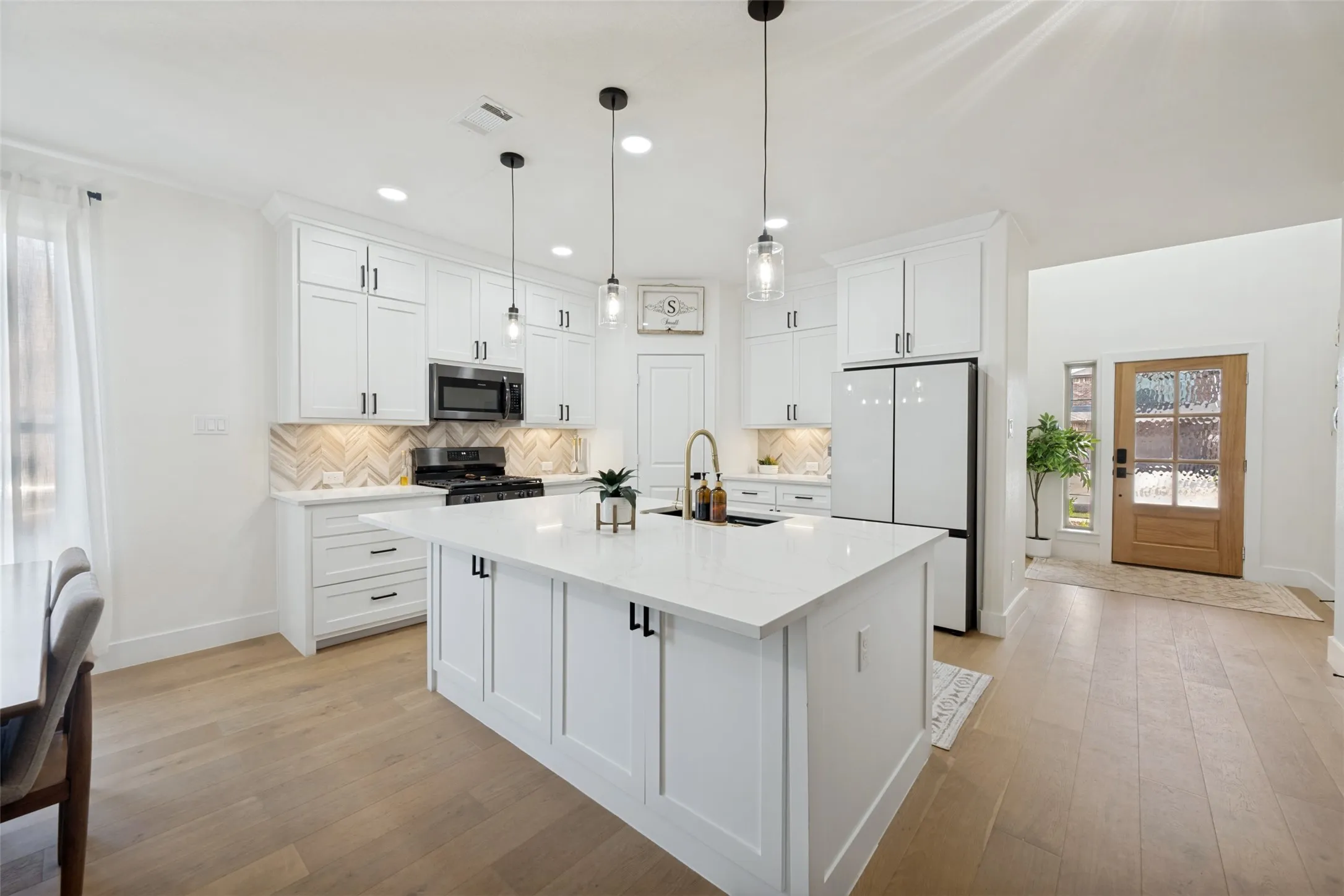 Open-concept kitchen with a large central island, white shaker cabinetry, stainless steel appliances, and a chevron-patterned tile backsplash