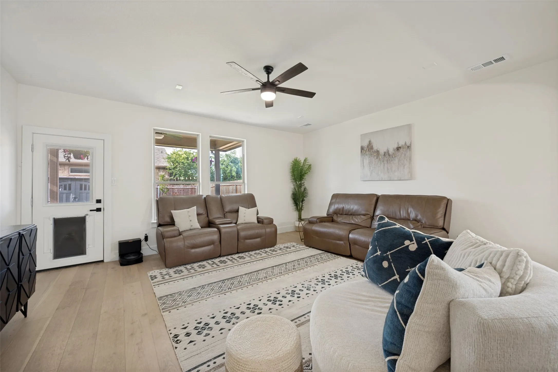 Spacious living area featuring light wood-finish flooring, a contemporary ceiling fan, recessed lighting, and multiple windows