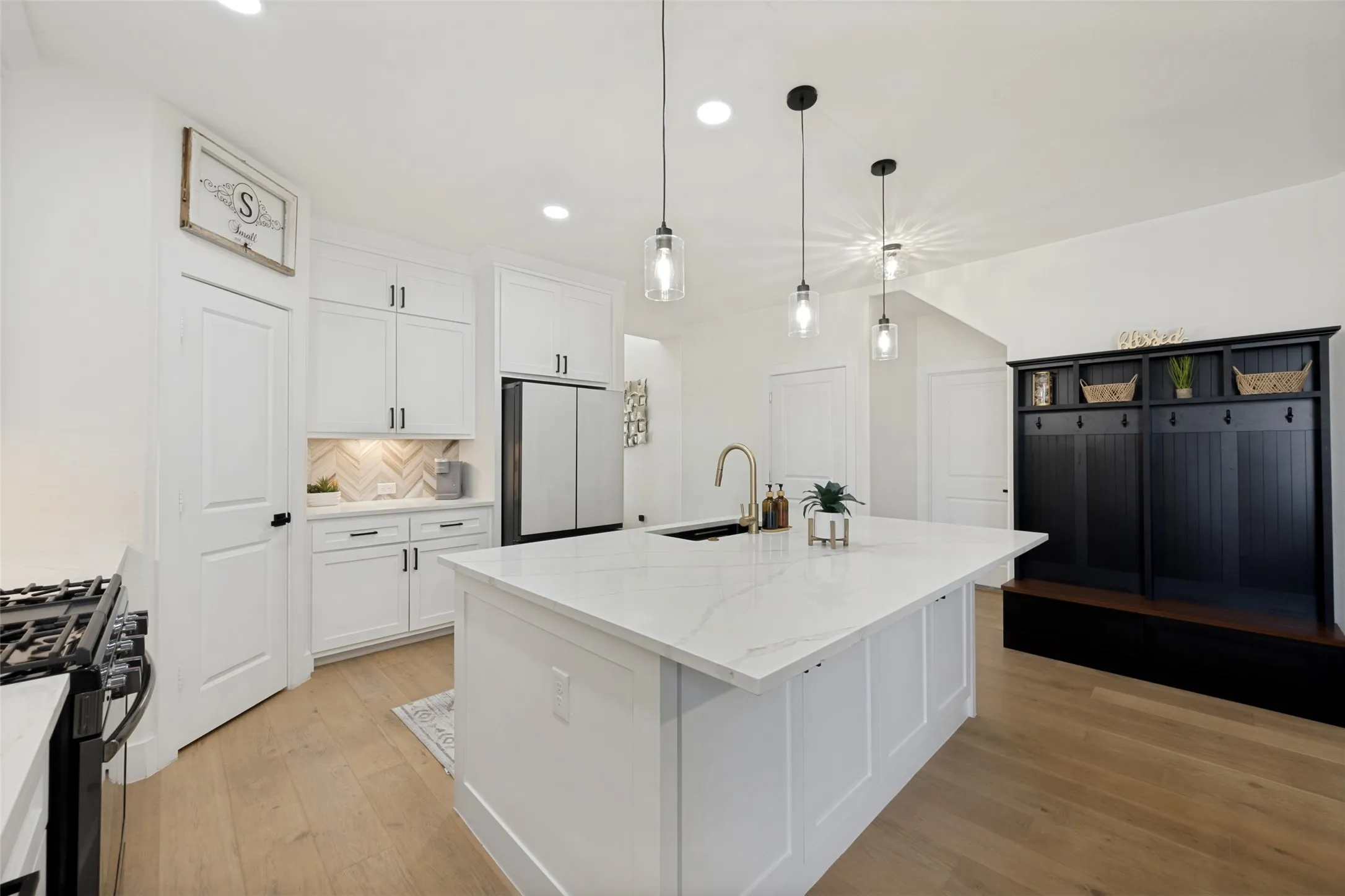 Spacious kitchen featuring an expansive central island with a gold-finish faucet and undermount sink, white cabinetry with black hardware, and wood-finish flooring