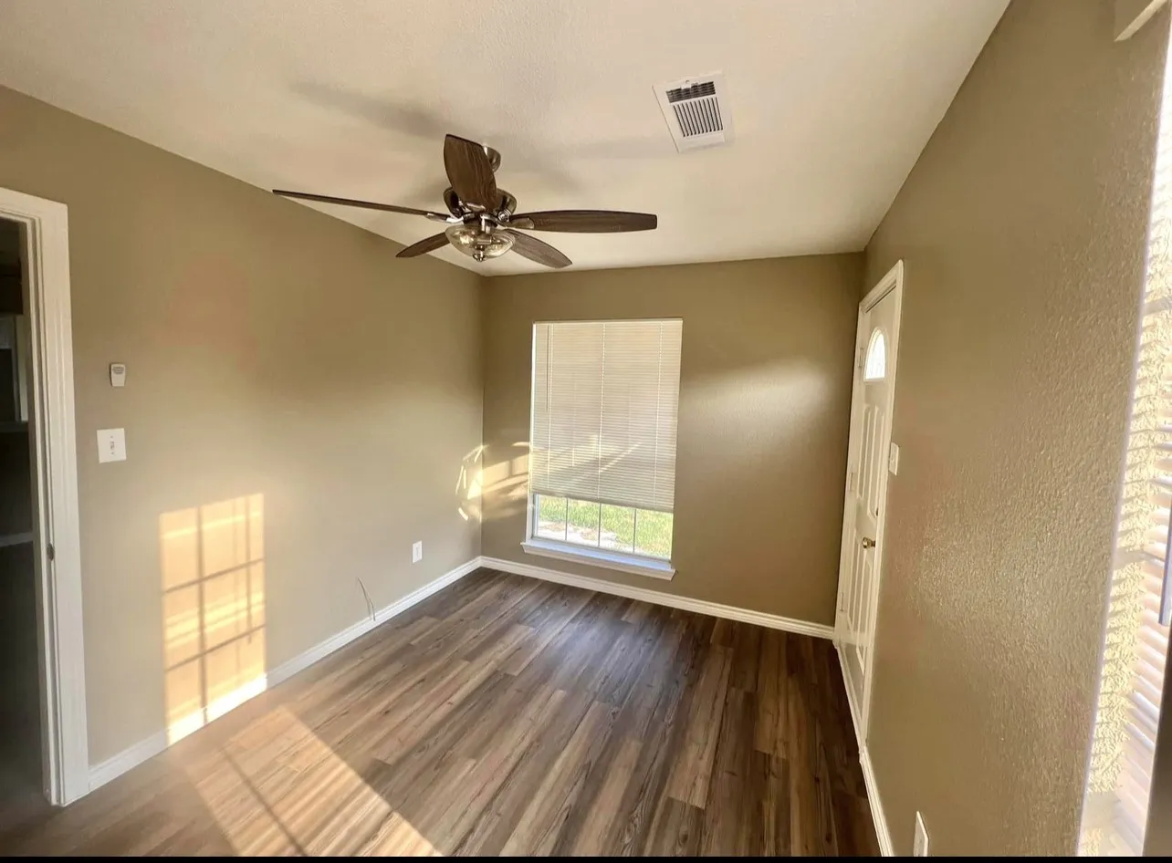 Warmly toned interior with wood-finish flooring, a ceiling fan, and window with blinds