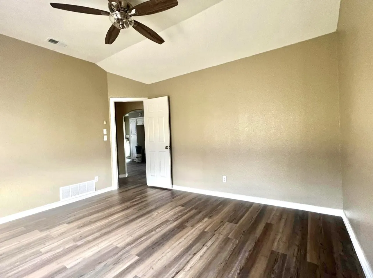 Vaulted ceiling with a ceiling fan, wood-finish flooring, neutral wall paint, and white trim