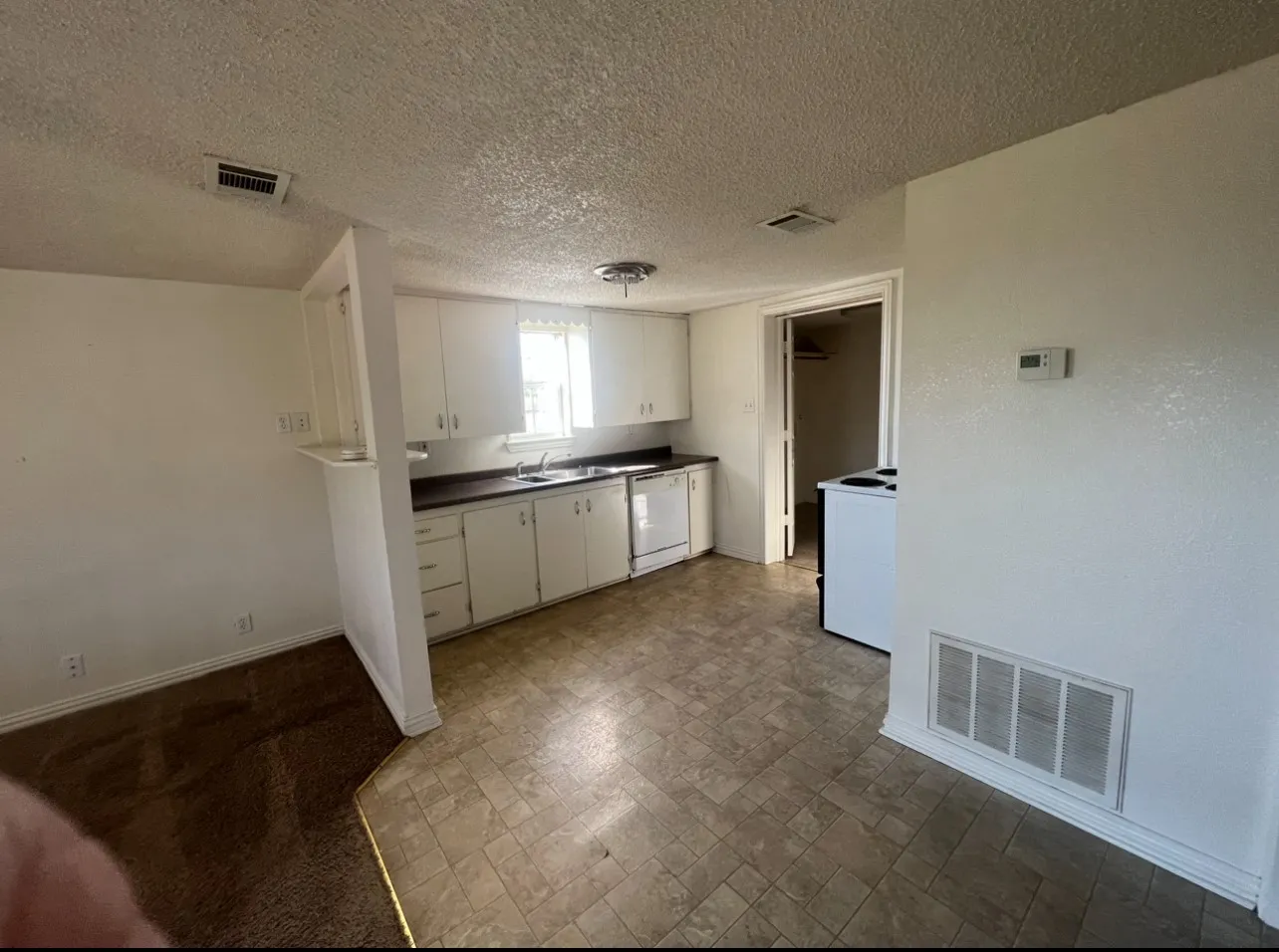 Kitchen area featuring white cabinetry, dark countertops, a double basin sink, and a white dishwasher