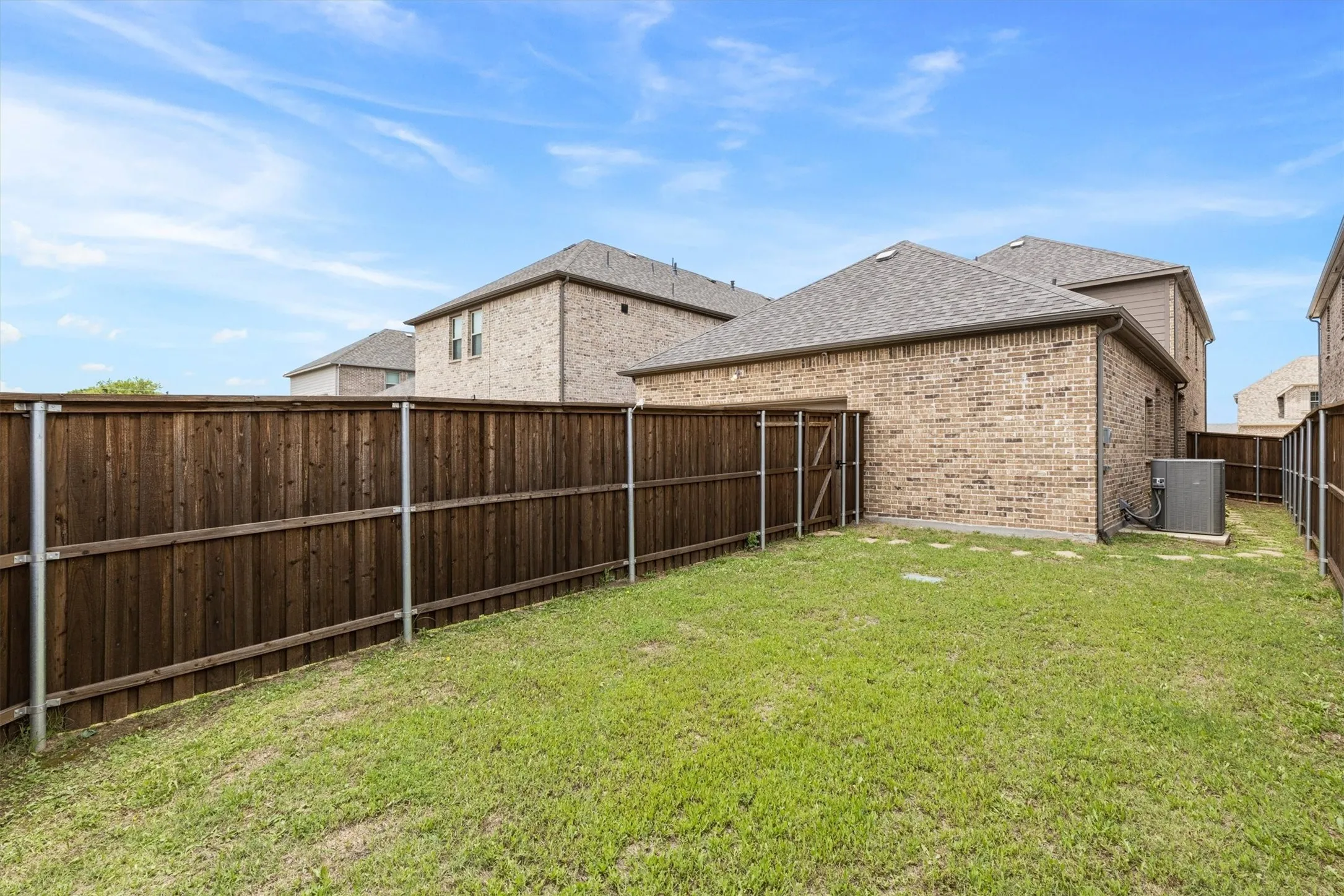 Fenced backyard featuring a manicured lawn, brick exterior, and a side access gate