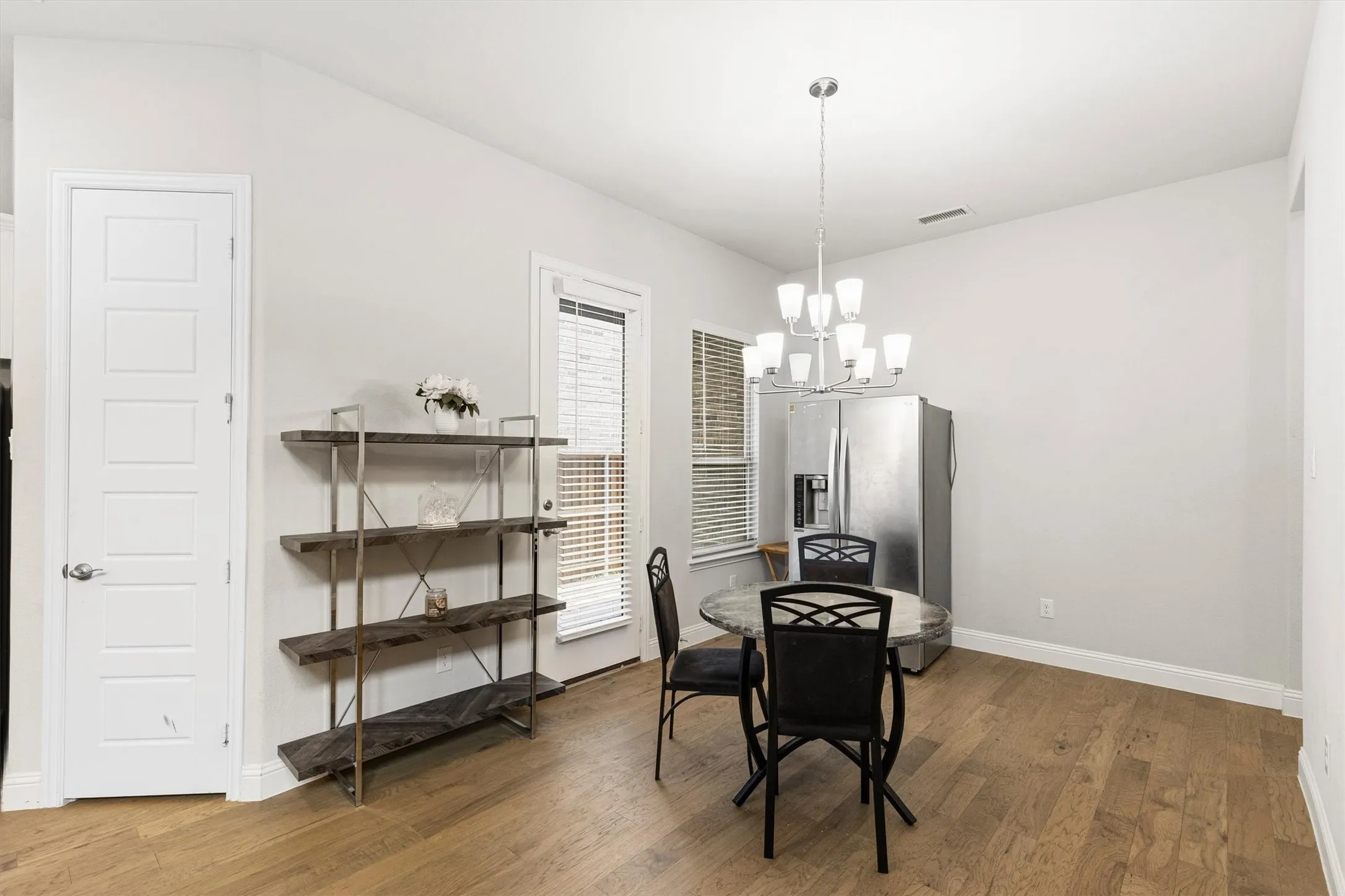 Spacious dining area featuring wood-finish flooring, a contemporary chandelier, and a large window with blinds