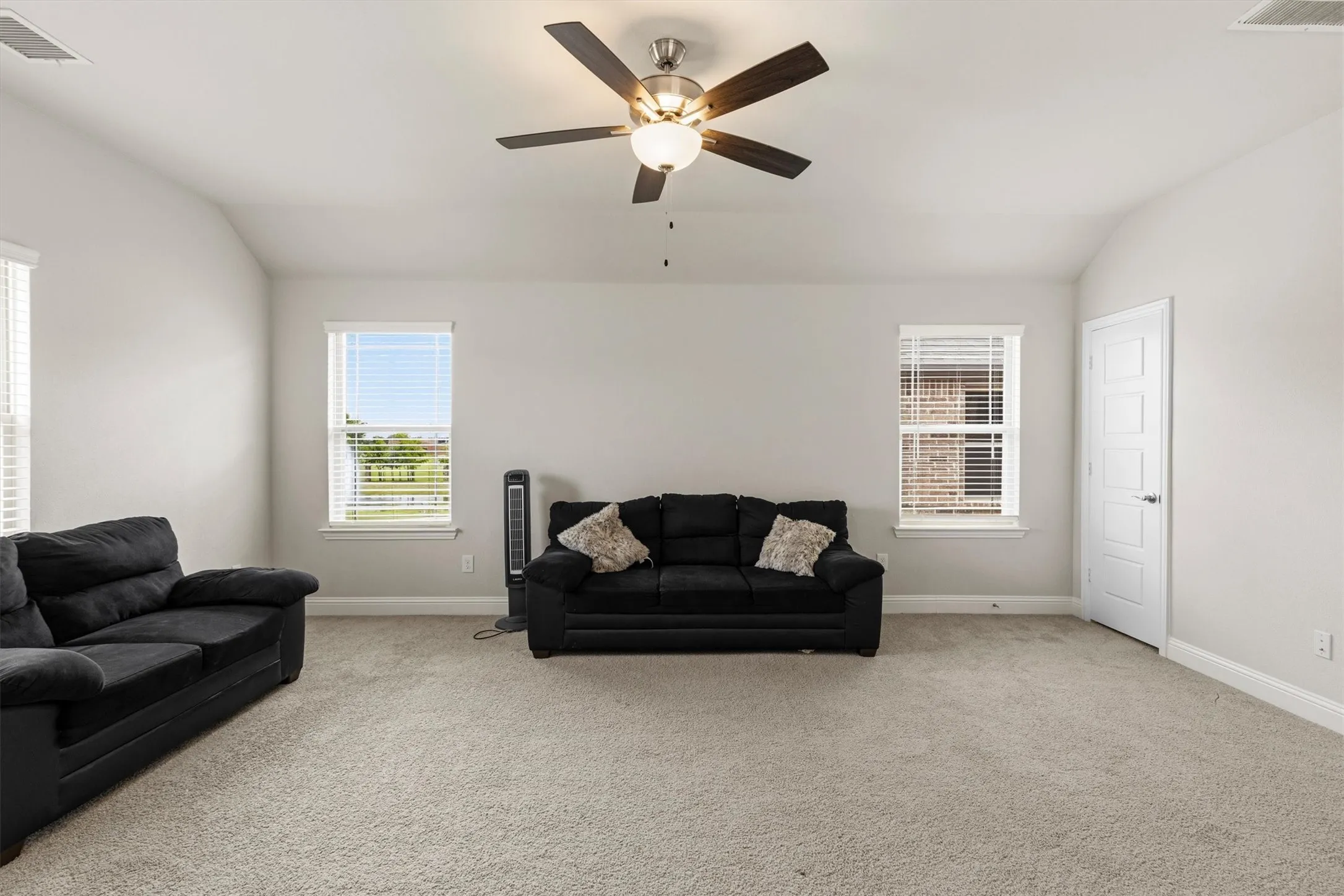 Spacious room featuring vaulted ceilings, light gray wall paint, and light-colored carpet flooring