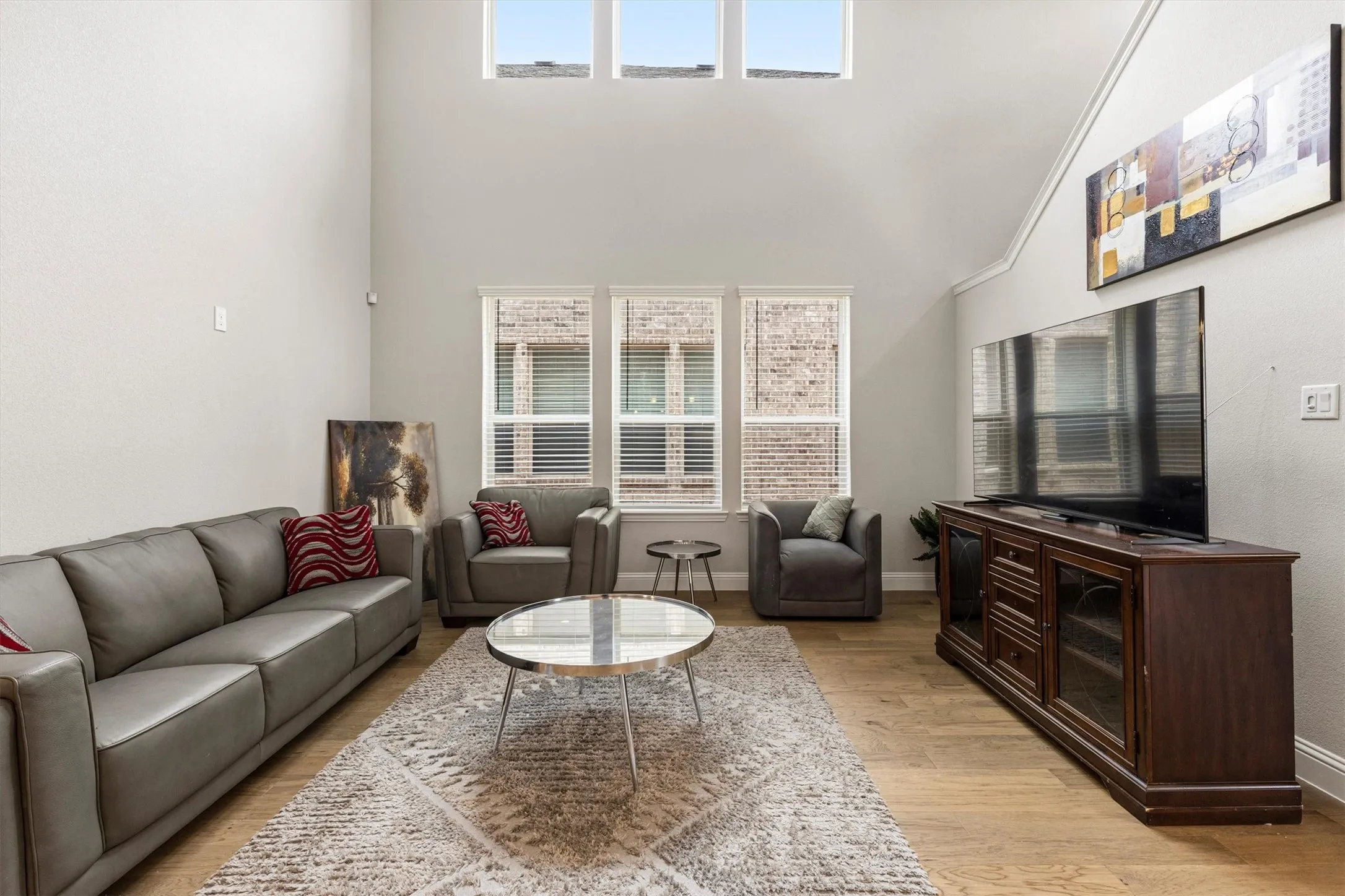 Vaulted ceiling living area featuring multiple windows, wood-finish flooring, and light-toned walls