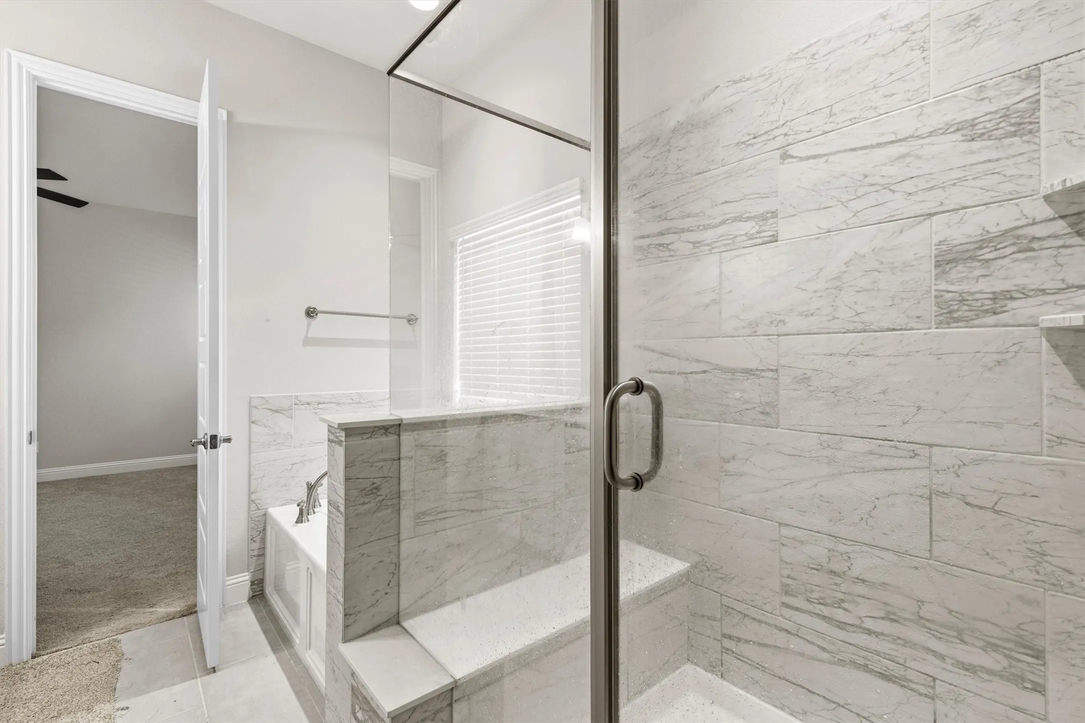 Walk-in shower with clear glass enclosure, integrated bench seating, and light-toned tilework