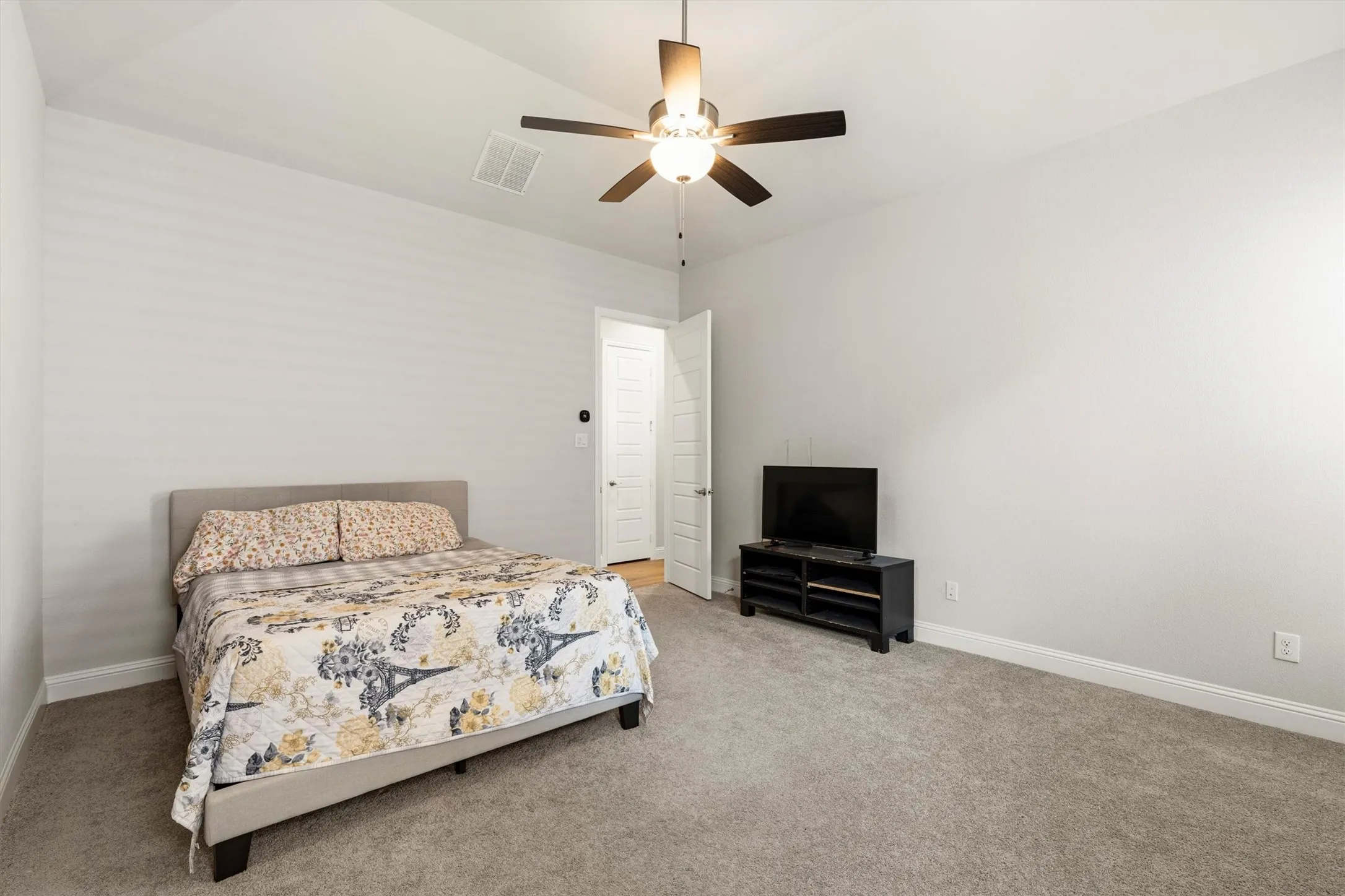 Spacious interior room featuring a vaulted ceiling with a ceiling fan, light gray wall paint, and gray carpet flooring