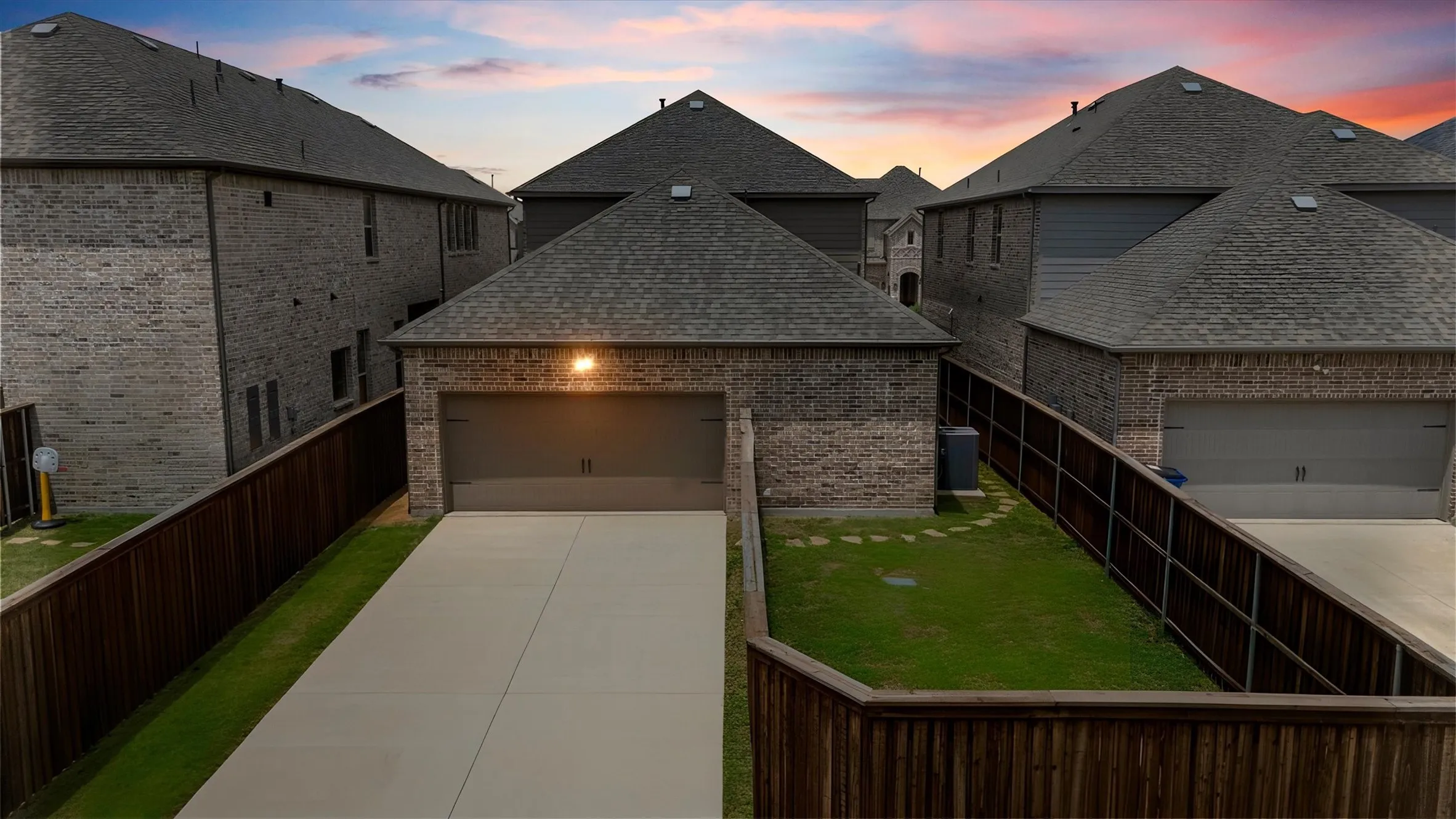 Private fenced backyard with a manicured lawn, stone stepping path, and extended concrete driveway leading to an attached garage