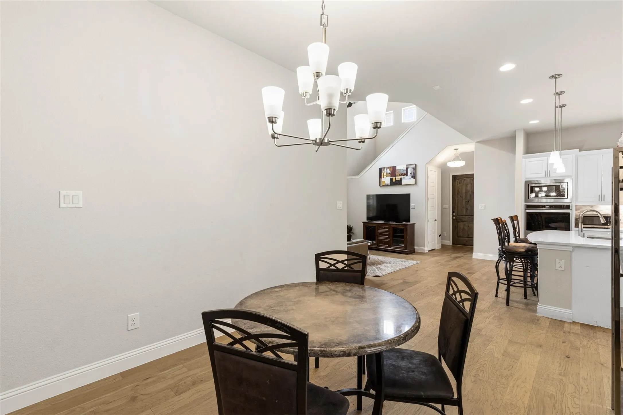 Open-concept living space featuring wood-finish flooring, a contemporary chandelier, a kitchen island with pendant lighting, white cabinetry, and built-in stainless steel appliances