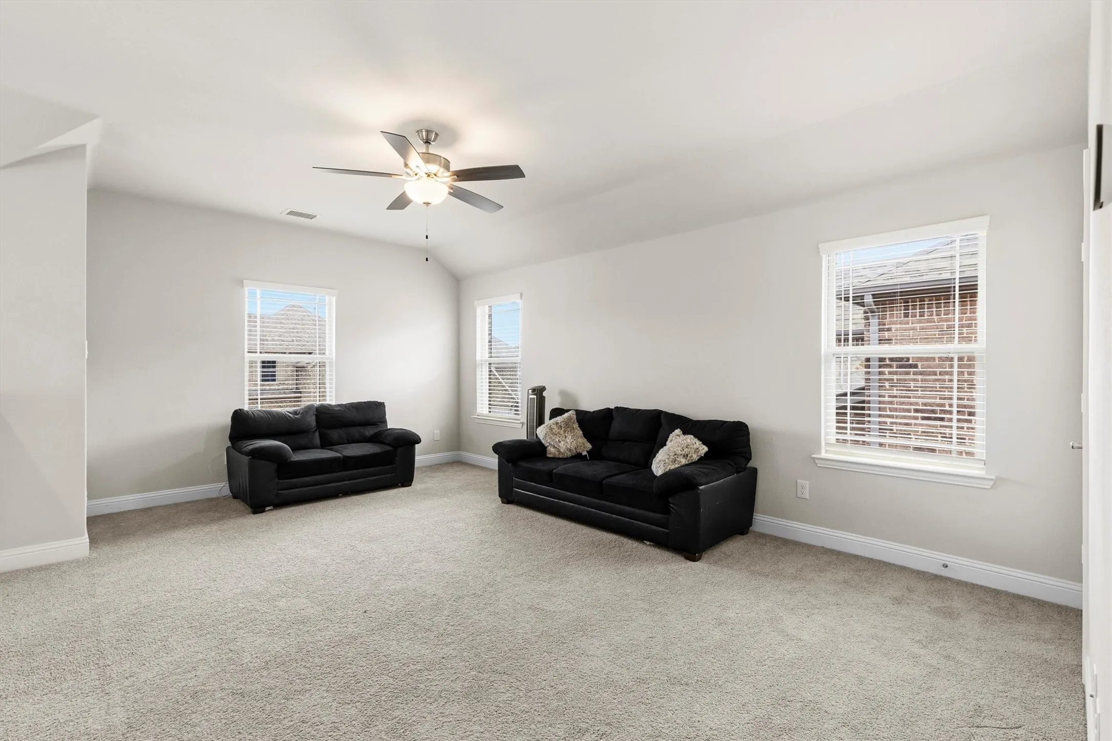 Spacious room featuring carpet flooring, multiple windows with blinds, a vaulted ceiling, and a ceiling fan with integrated lighting