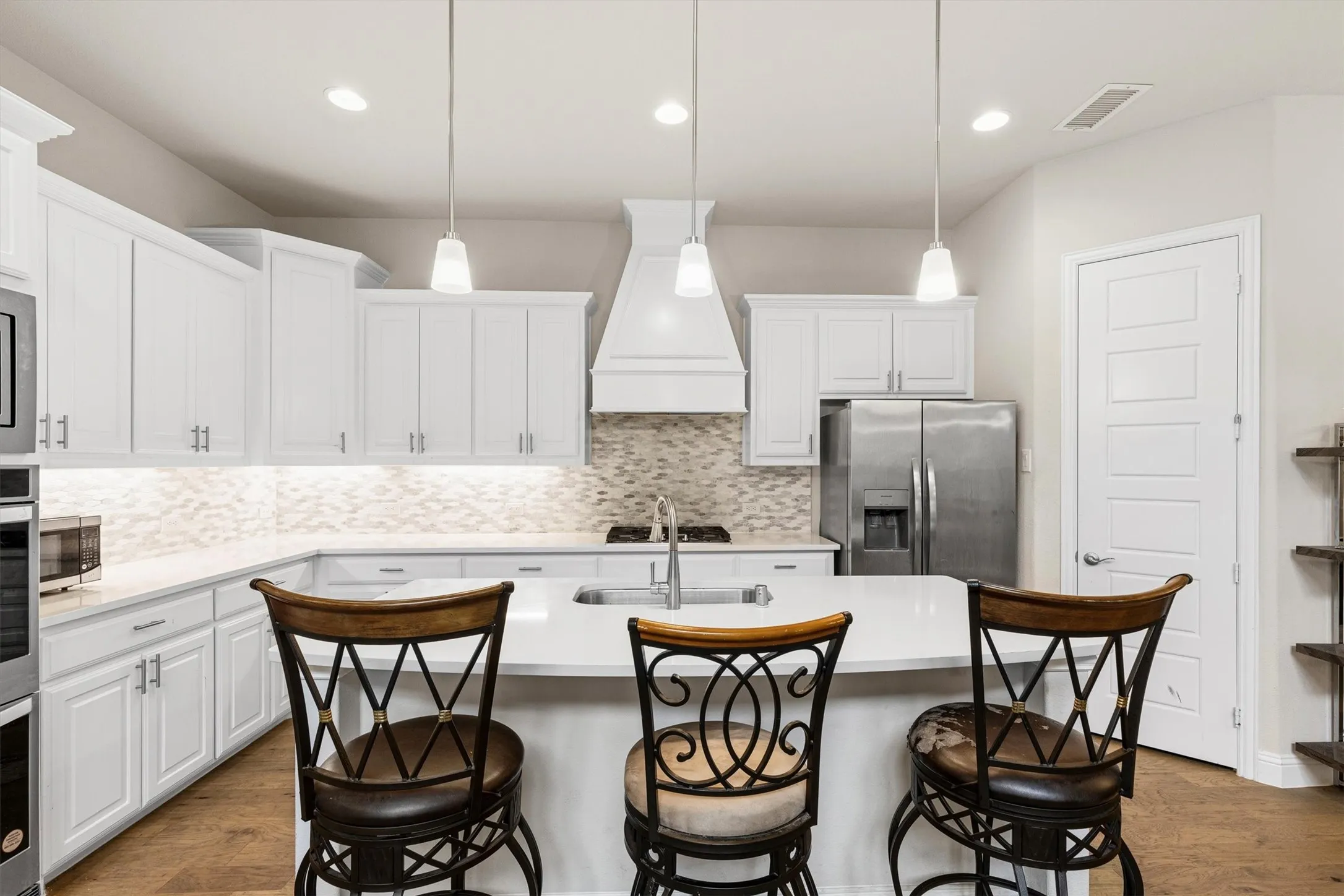 Spacious kitchen featuring an expansive island, white shaker cabinetry, stainless steel appliances, pendant lighting, and a decorative tile backsplash
