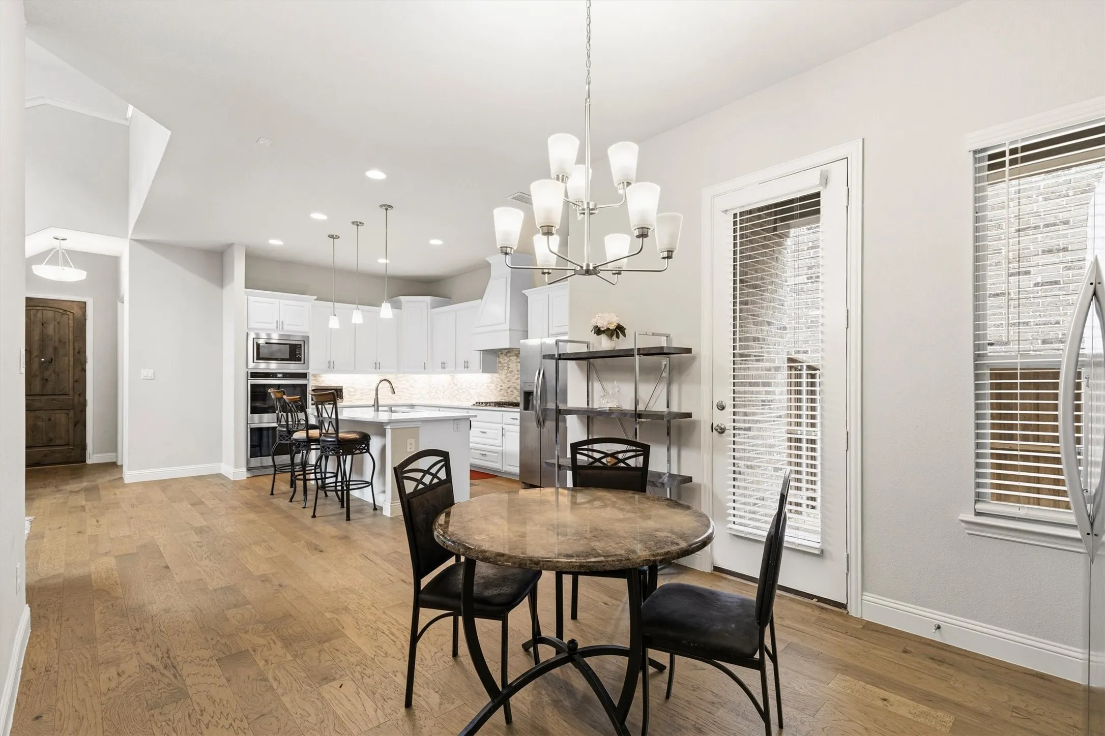 Open-concept kitchen and dining area featuring light wood-finish flooring, white cabinetry, stainless steel appliances, and a central island with pendant lighting