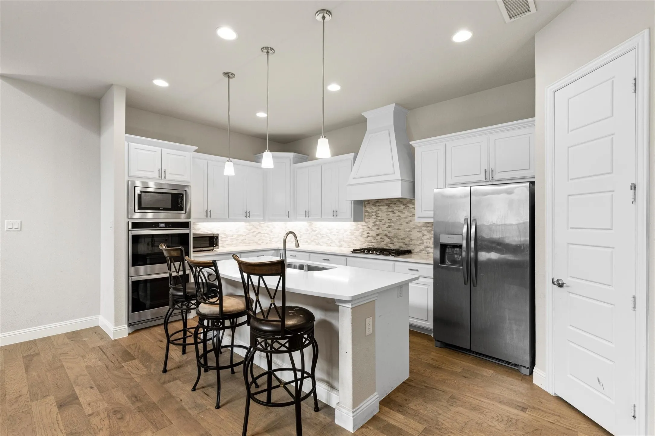 Modern kitchen featuring white cabinetry, stainless steel appliances, a center island with pendant lighting, a tile backsplash, and wood-finish flooring