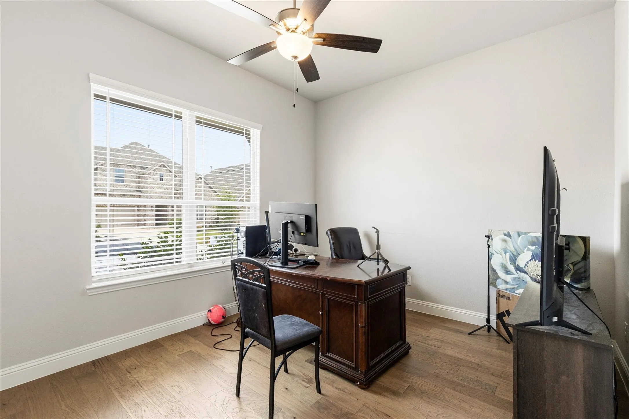 Room with wood-finish flooring, a ceiling fan with integrated lighting, and a large window with blinds