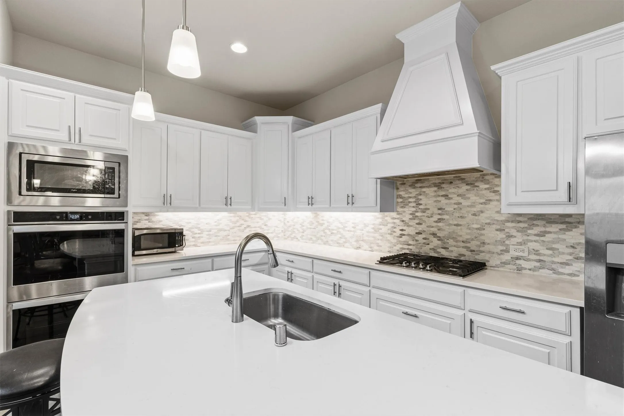 Contemporary kitchen featuring white cabinetry, stainless steel appliances, a multi-tone tile backsplash, and a large central island with an undermount sink and gooseneck faucet