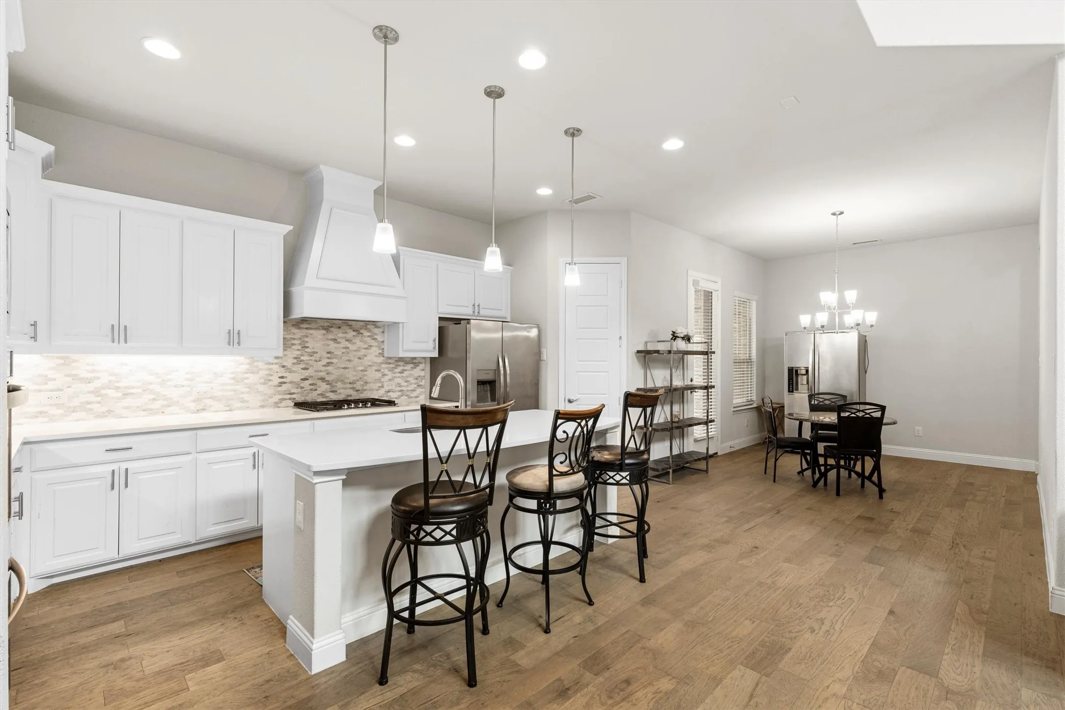 Open-concept kitchen featuring white cabinetry, a large kitchen island with pendant lighting, stainless steel appliances, a tiled backsplash, and wood-finish flooring