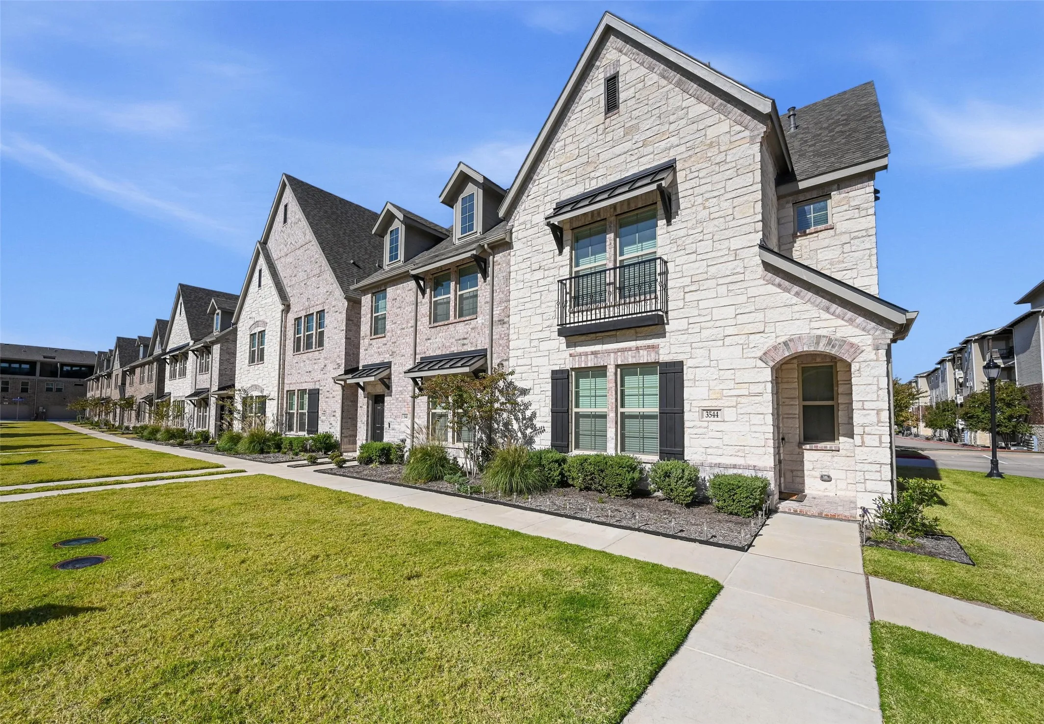 French provincial home featuring a front lawn, a residential view, stone siding, and a balcony