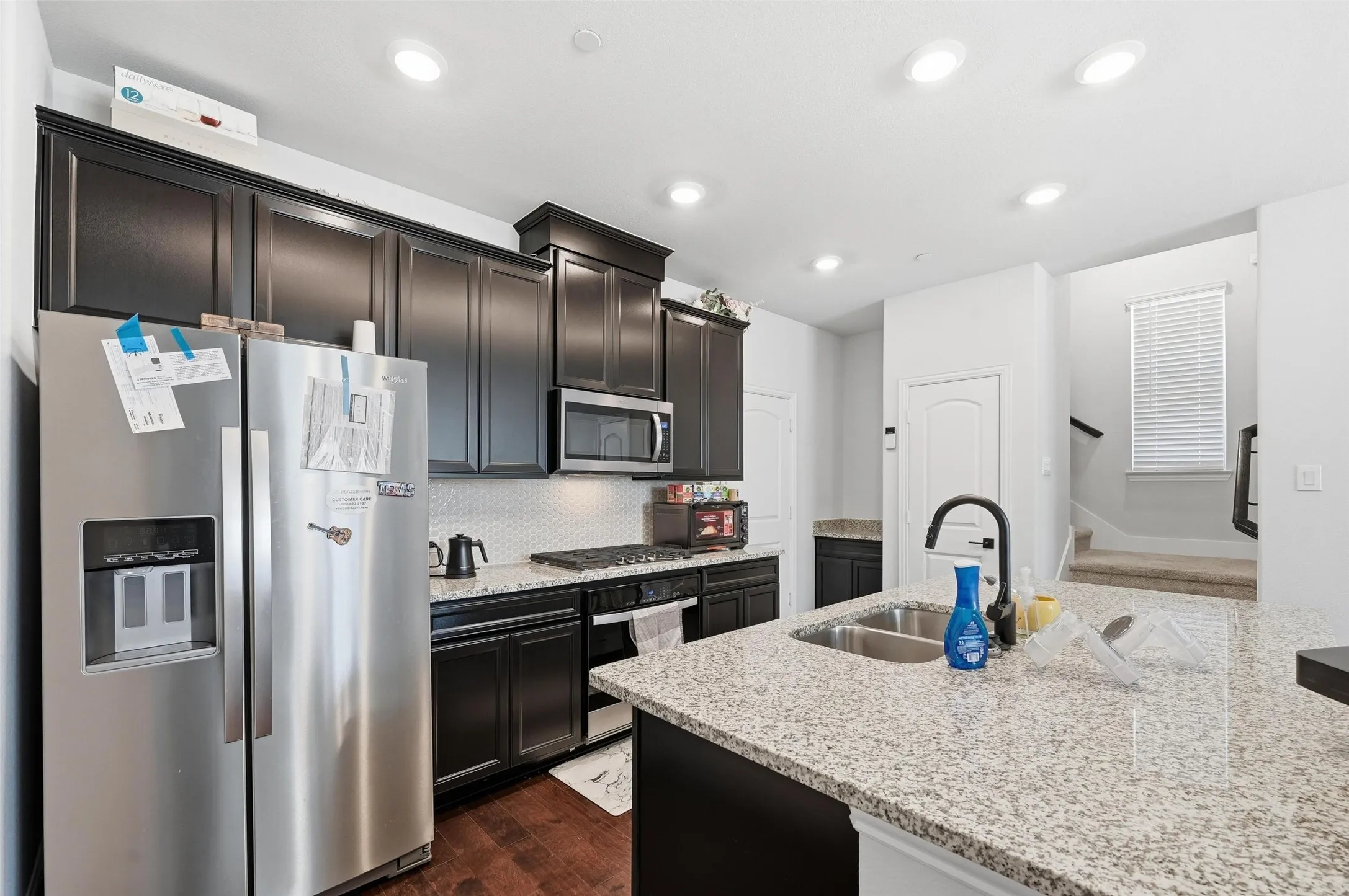 Kitchen featuring appliances with stainless steel finishes, tasteful backsplash, light stone counters, dark wood-type flooring, and recessed lighting