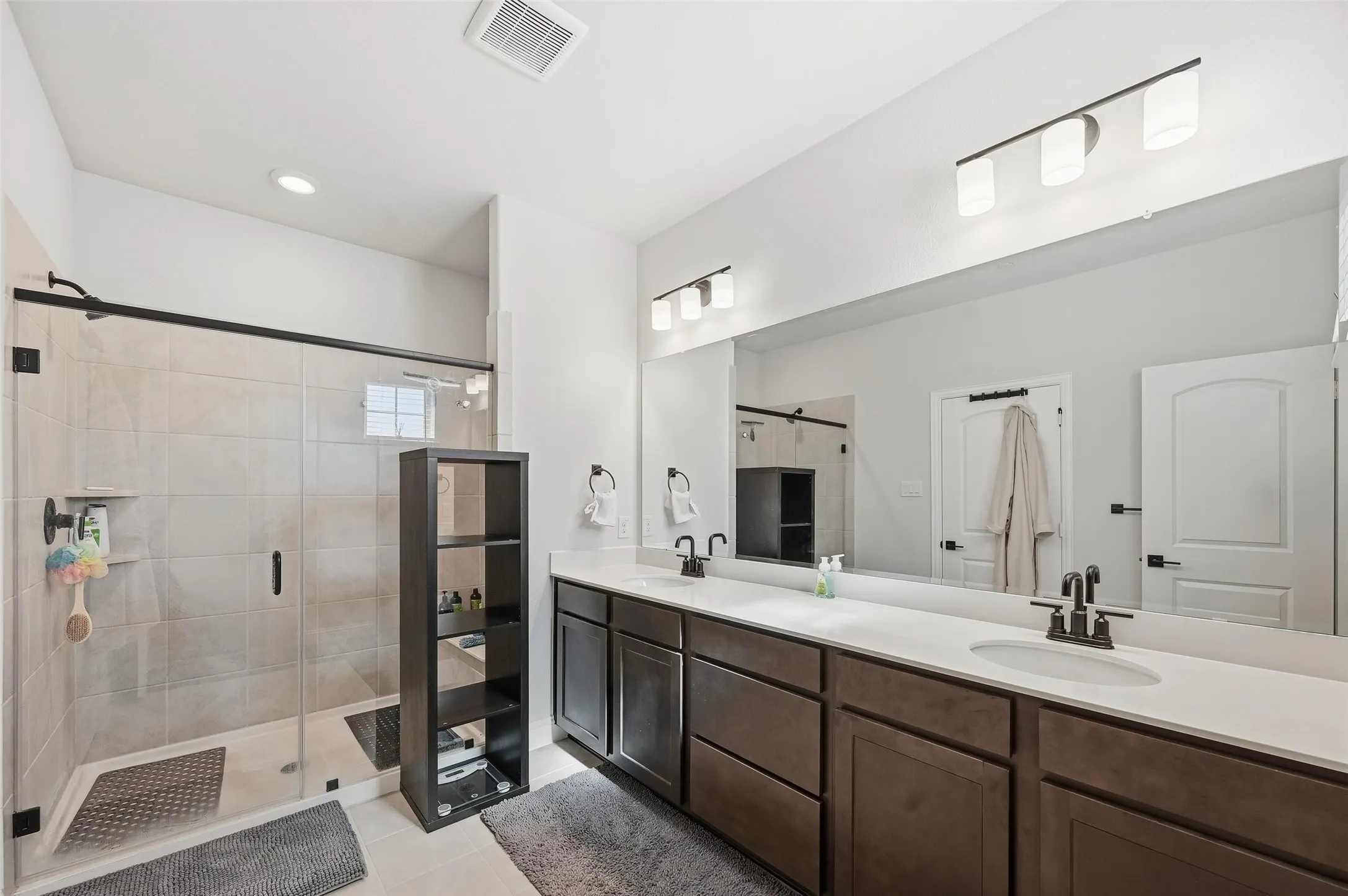Bathroom featuring double vanity, light tile patterned floors, a shower stall, and recessed lighting