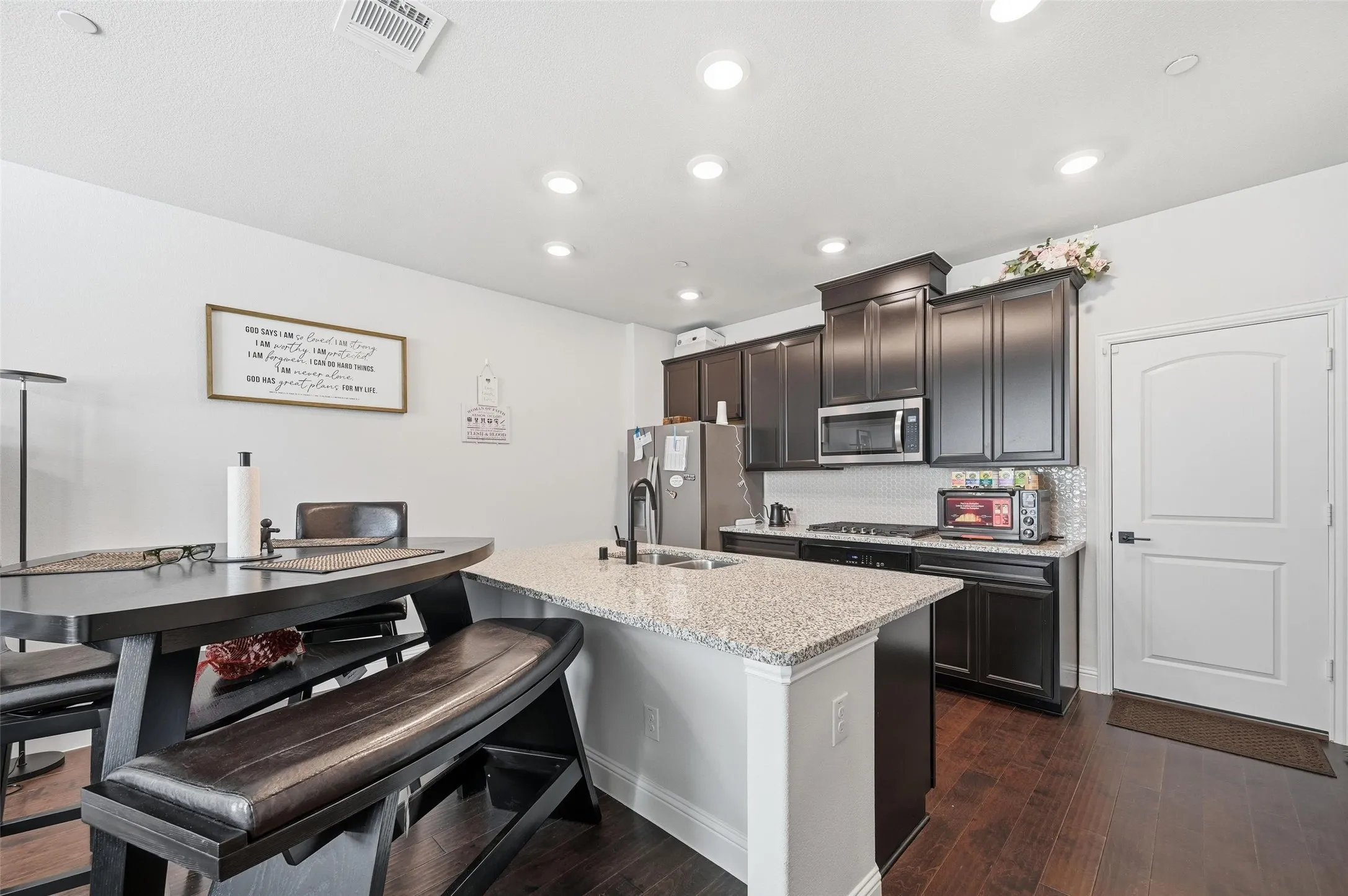 Kitchen featuring light stone counters, decorative backsplash, dark wood-style flooring, stainless steel appliances, and dark brown cabinetry