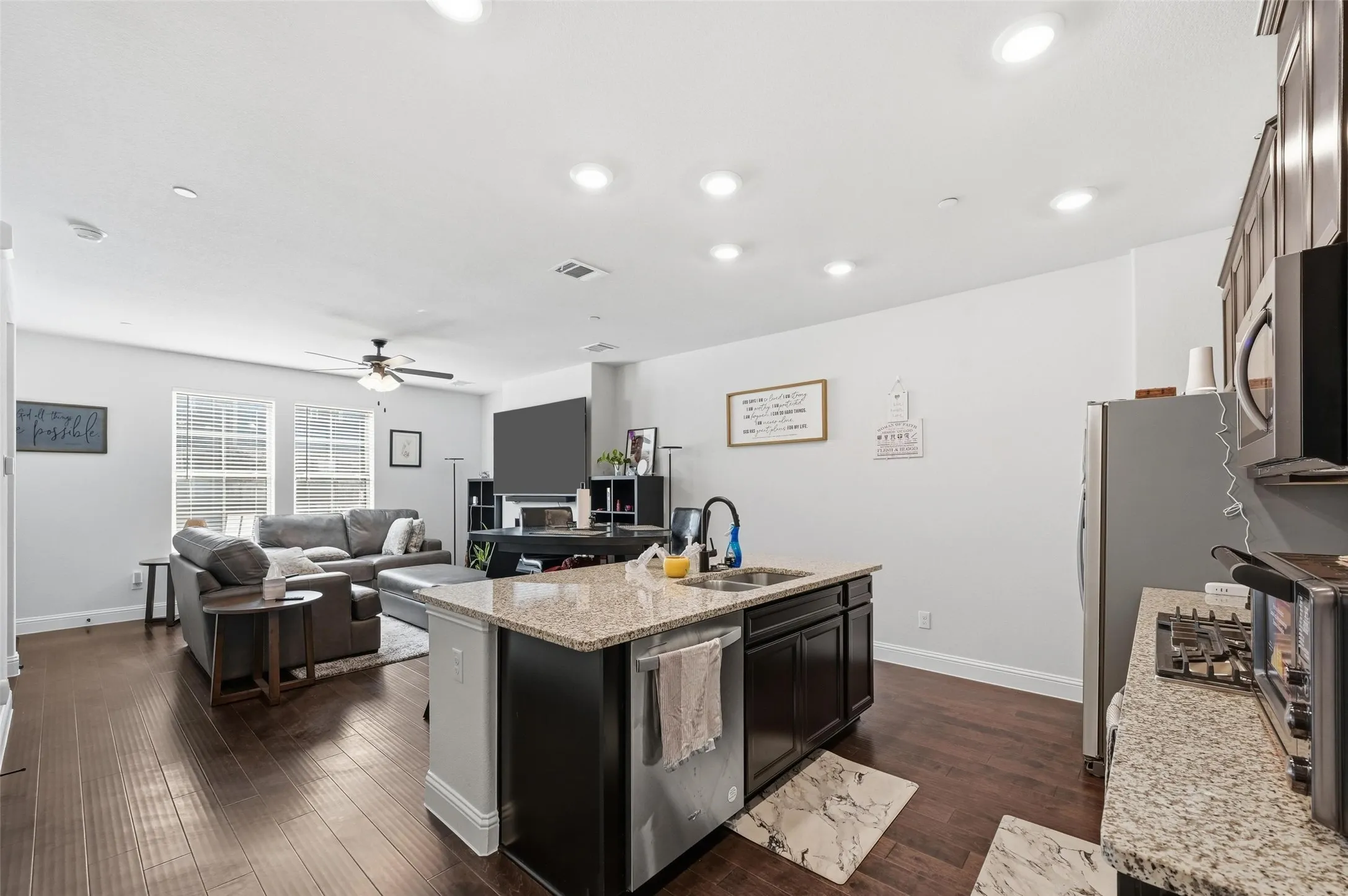 Kitchen with light stone countertops, a center island with sink, dark wood finished floors, open floor plan, and stainless steel appliances