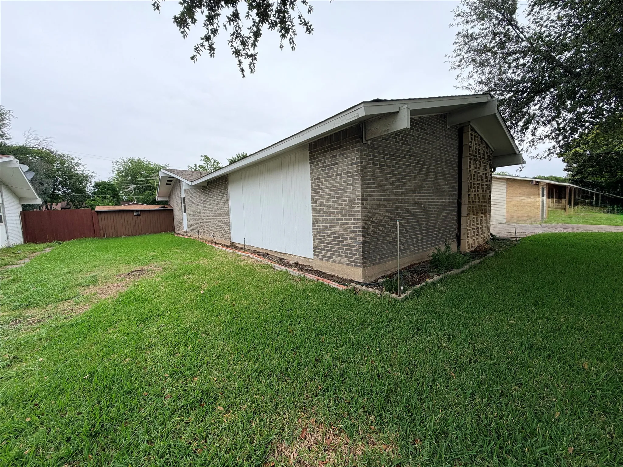 Side exterior featuring brick and white vertical siding, a pitched roofline, and a perimeter landscape bed