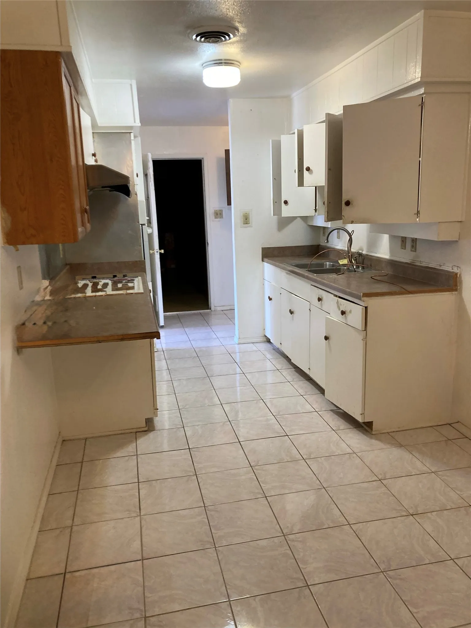 Galley kitchen featuring tile flooring, white cabinetry, a built-in cooktop, and a stainless steel sink with a single-handle faucet