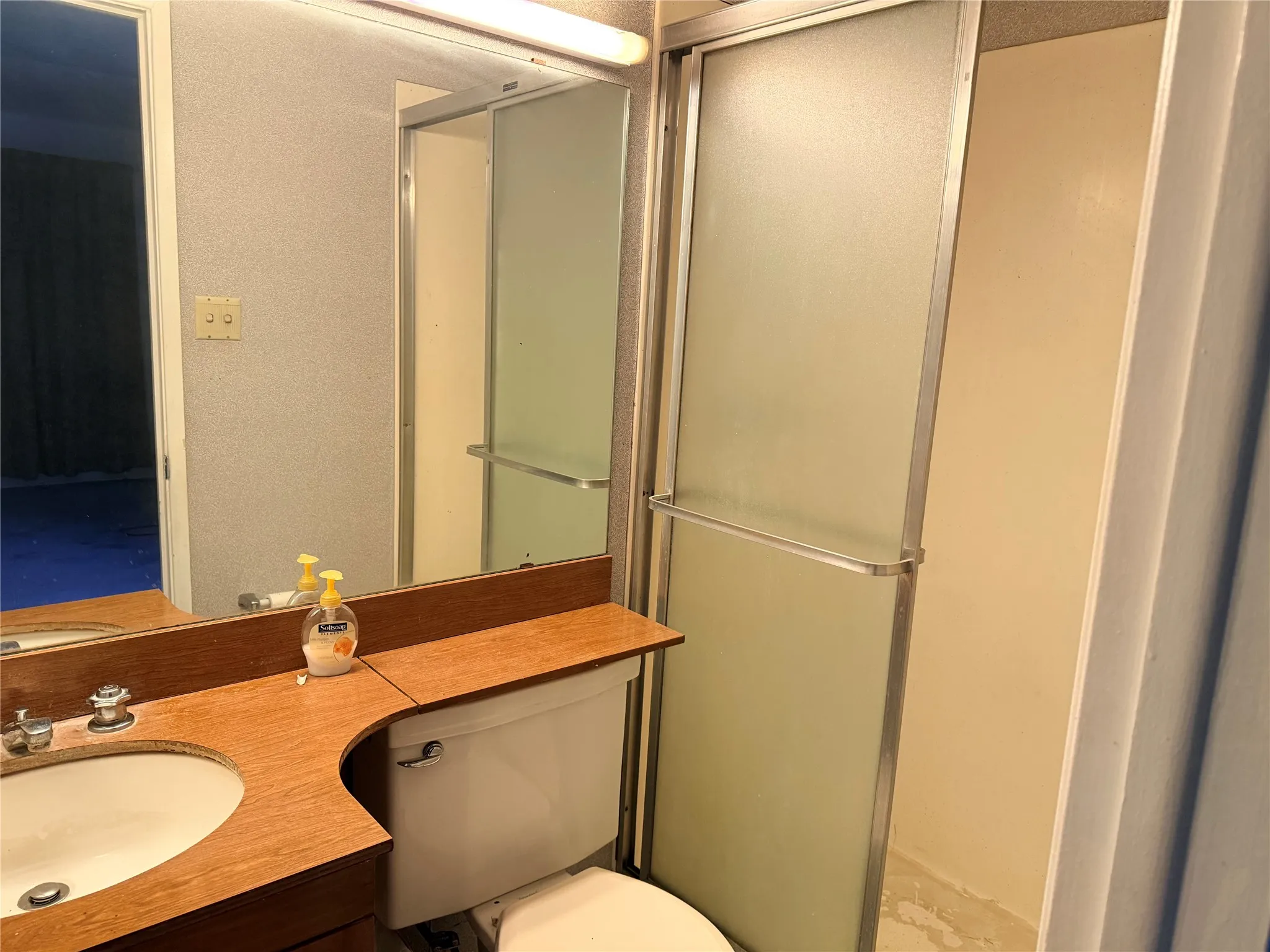 Bathroom featuring a wood-finish vanity with an integrated sink, a white toilet, and a shower enclosure with frosted glass sliding doors and a metal frame
