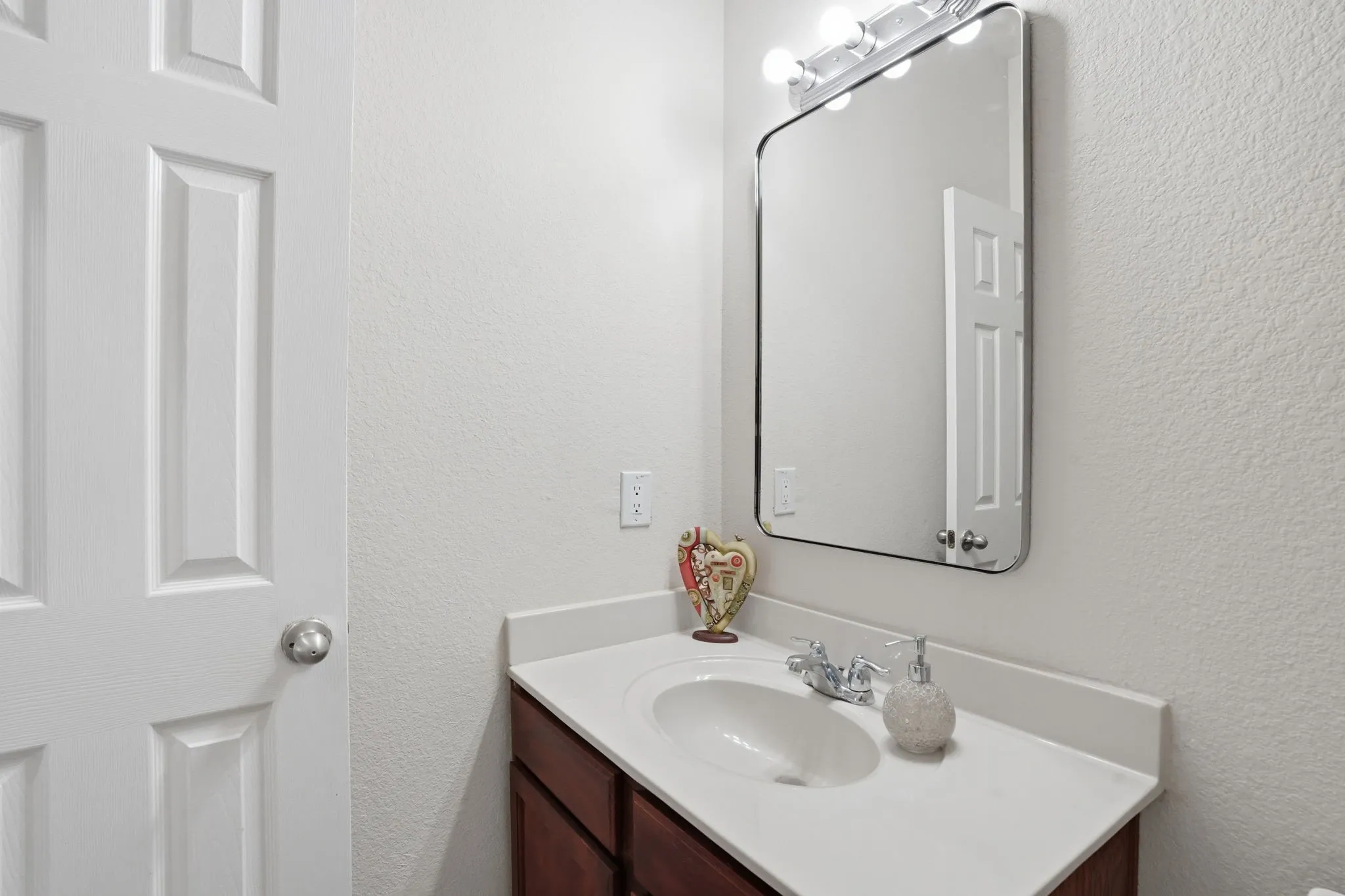 Bathroom vanity featuring a white countertop with an integrated sink, polished chrome faucet, and a mirror with overhead lighting