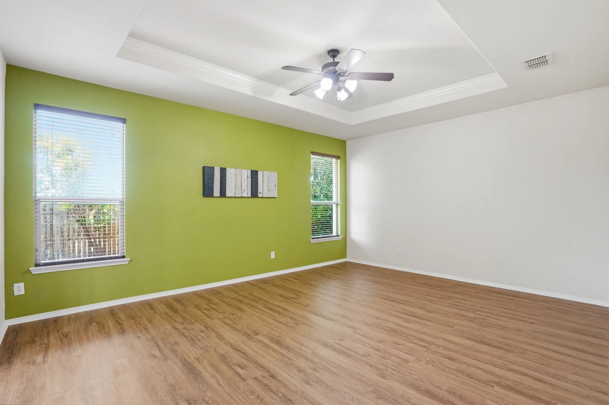 Spacious room featuring wood-finish flooring, a tray ceiling with crown molding, and a ceiling fan with integrated lighting