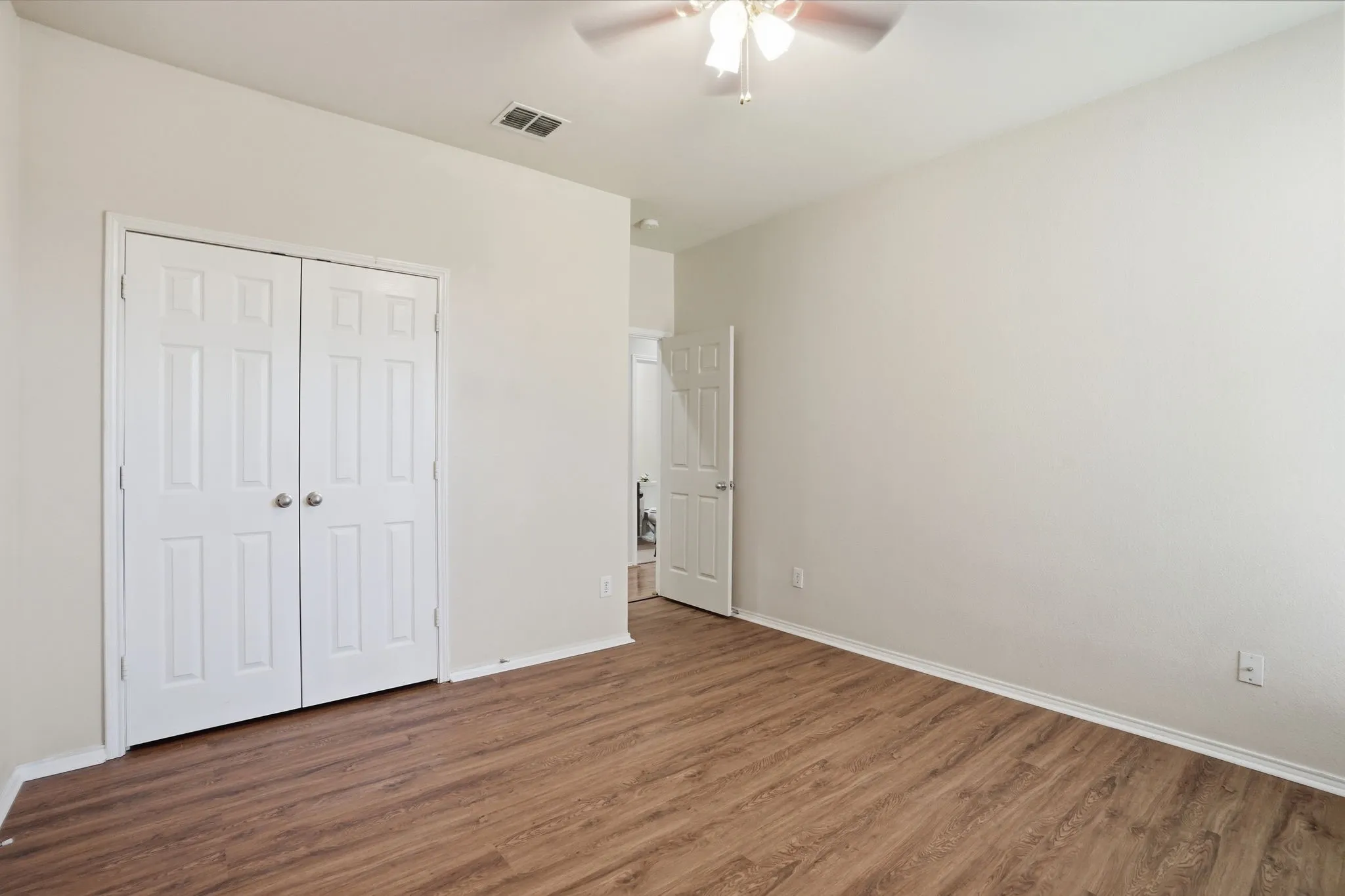 Room featuring wood-finish flooring, light-toned walls, white baseboards, and a ceiling fan