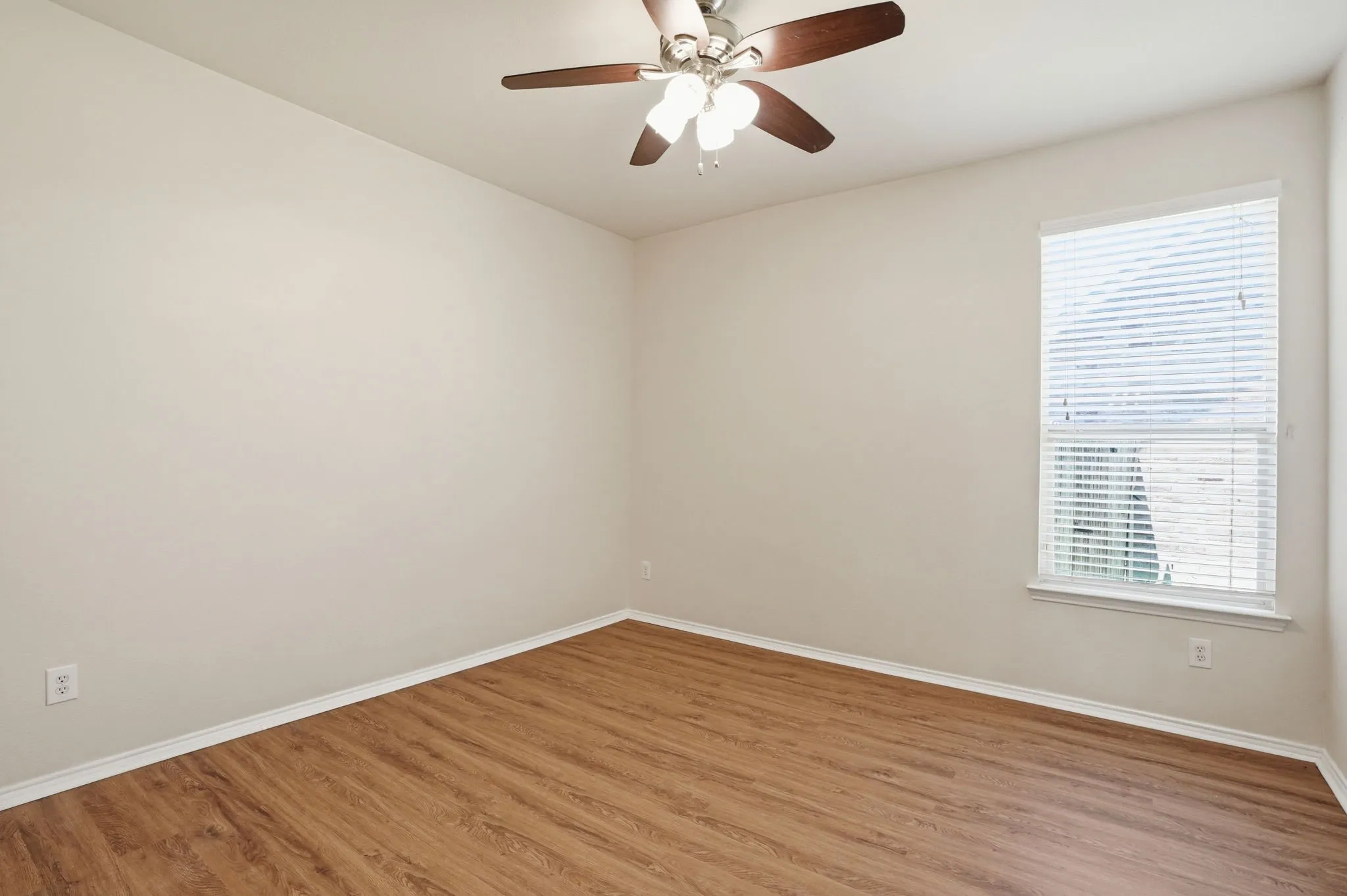 Neutral-toned room featuring wood-finish flooring, a ceiling fan with integrated lighting, and a window with horizontal blinds