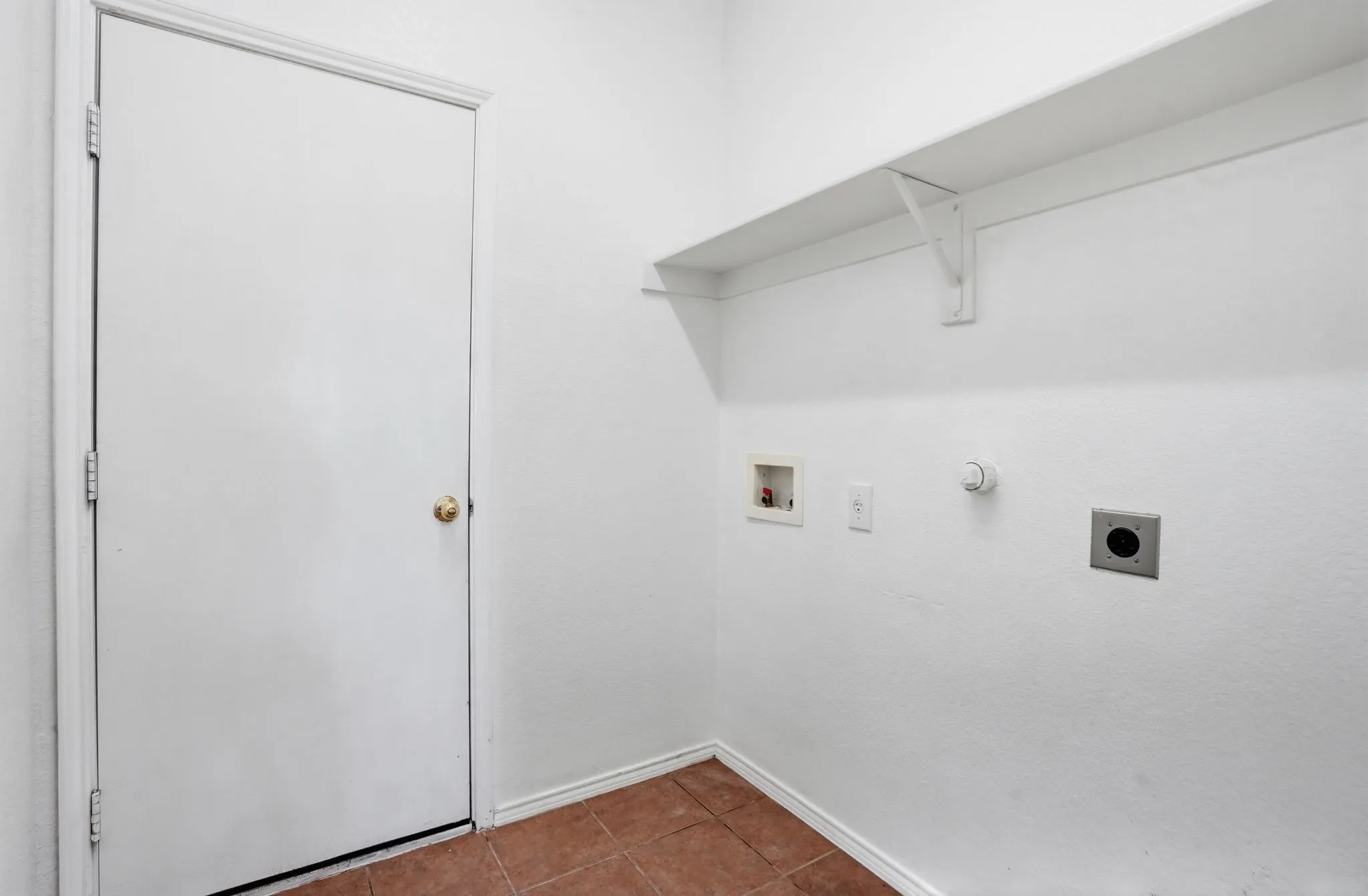 Dedicated utility space featuring a built-in wall shelf, tile flooring, and essential appliance hookups