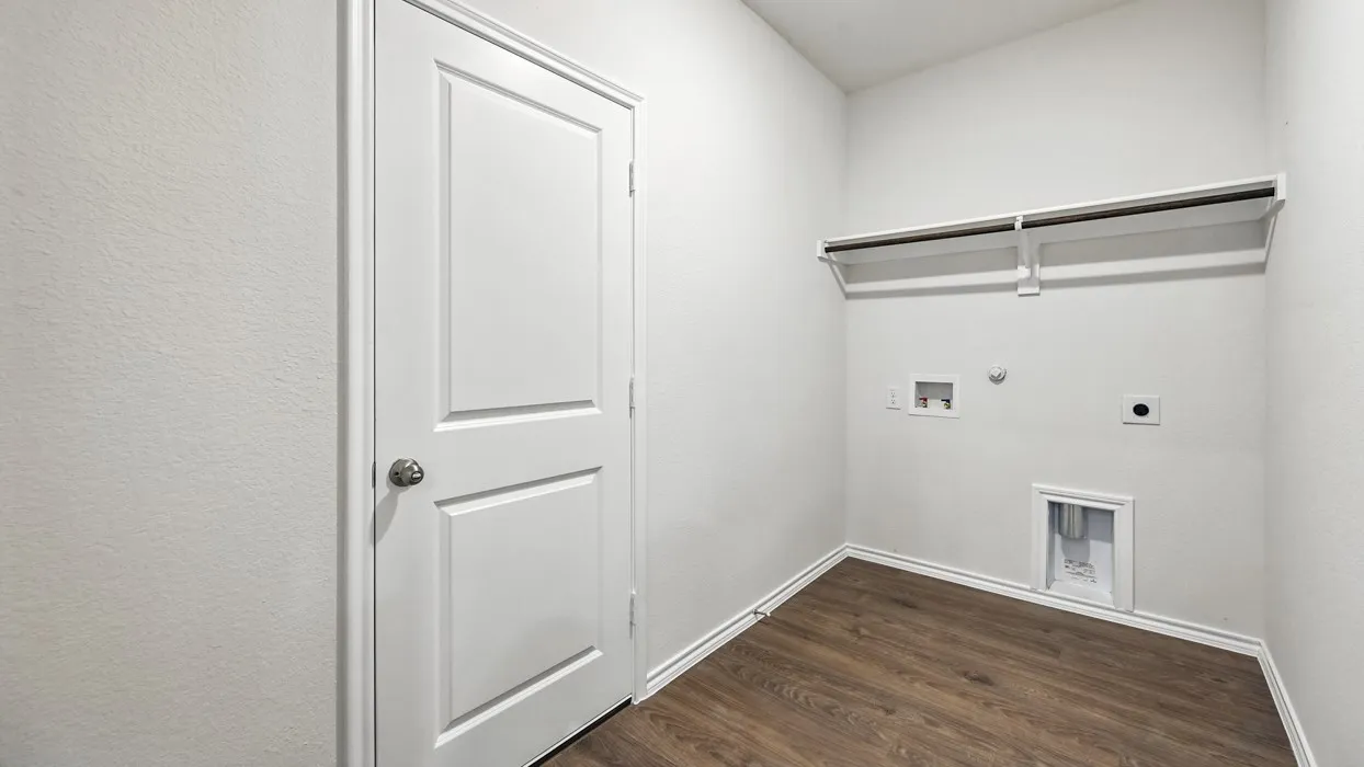 Dedicated laundry area featuring wood-finish flooring, crisp white walls, a two-panel interior door, and a built-in shelving unit with a hanging rod