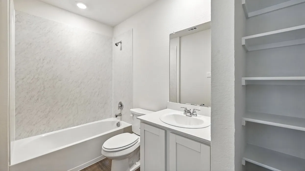 Bathroom featuring a white bathtub with a textured surround, a vanity with a white countertop and integrated sink, a large mirror, and built-in shelving