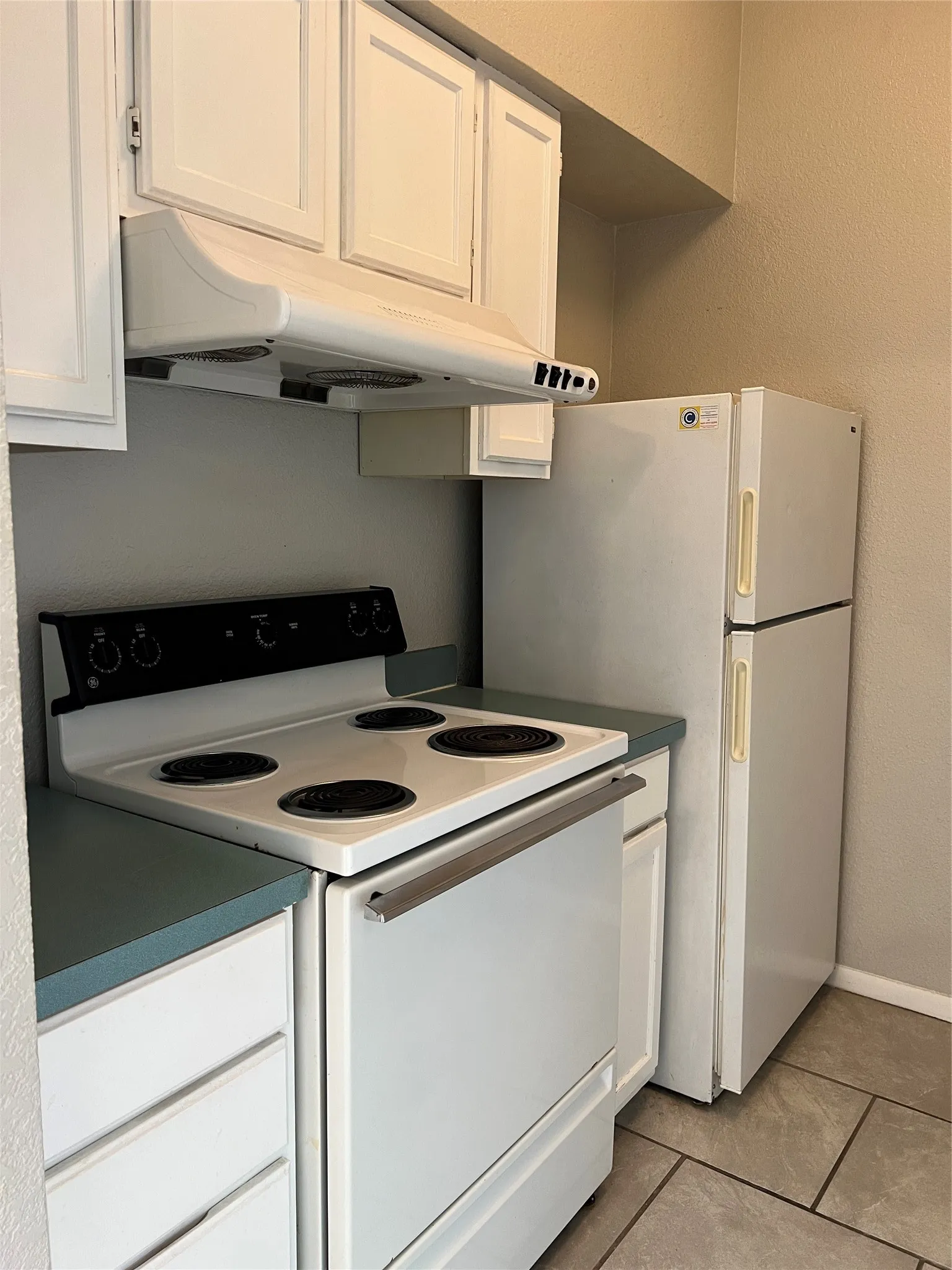 White cabinetry with integrated range hood, white electric range, white refrigerator, and gray tile flooring