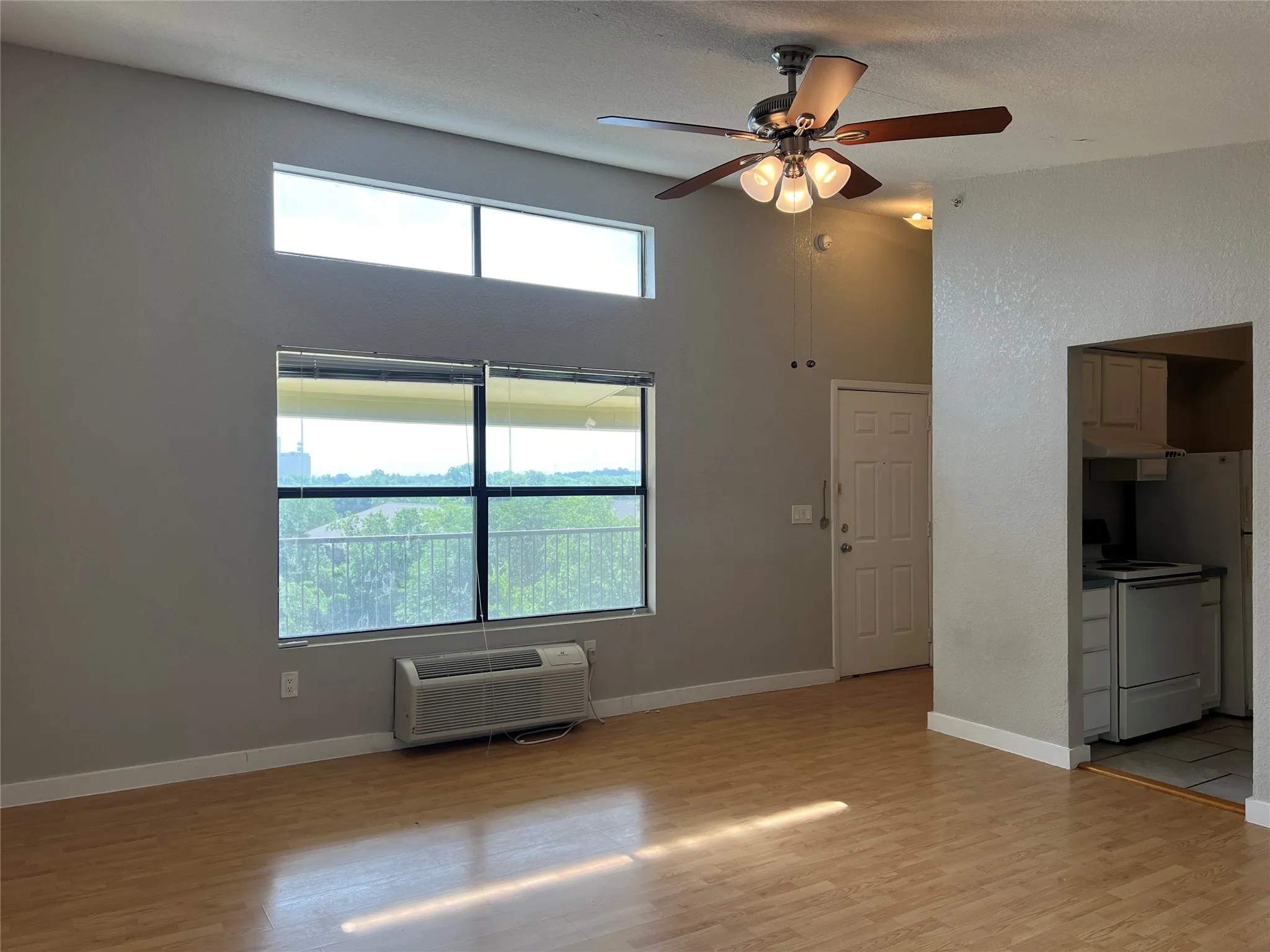 Wood-finish flooring, high ceilings, large windows, and a ceiling fan with integrated lighting