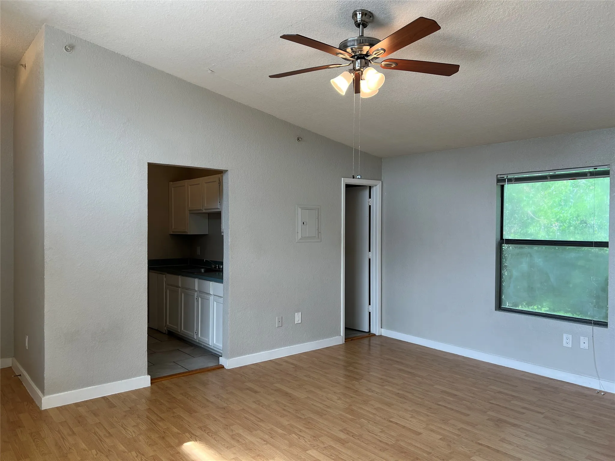 Vaulted ceiling, wood-finish flooring, ceiling fan with integrated lighting, natural light through a large window, kitchen with white cabinetry