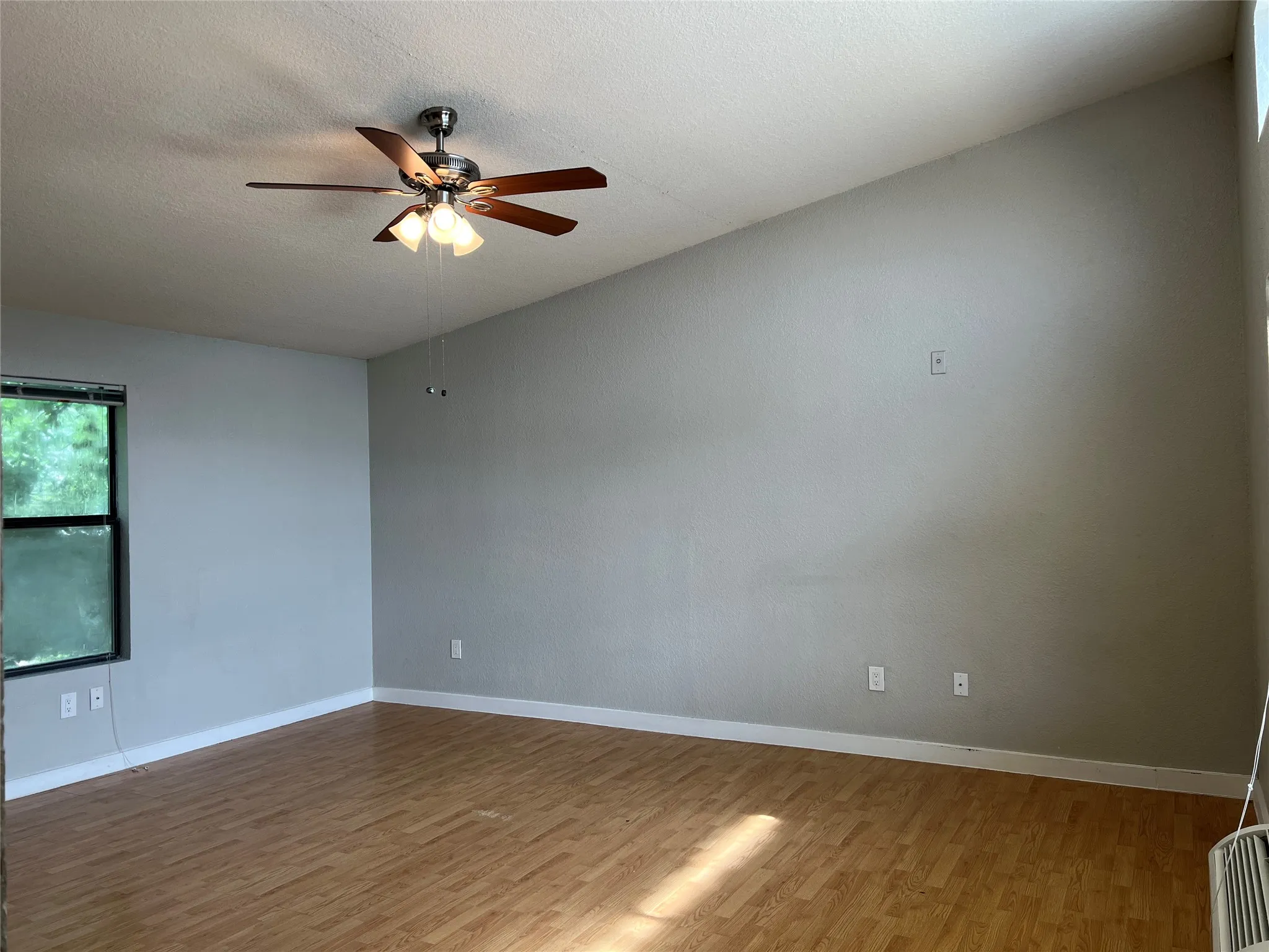 Vaulted ceiling with a ceiling fan and light fixture, wood-finish flooring, and a single pane window