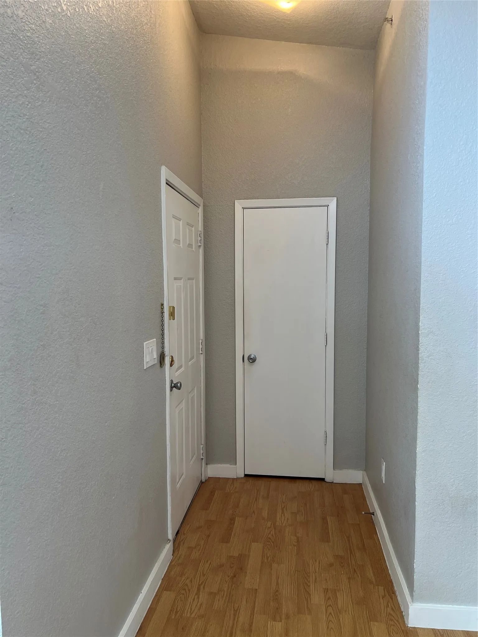 Wood-finish flooring with white baseboards and textured walls