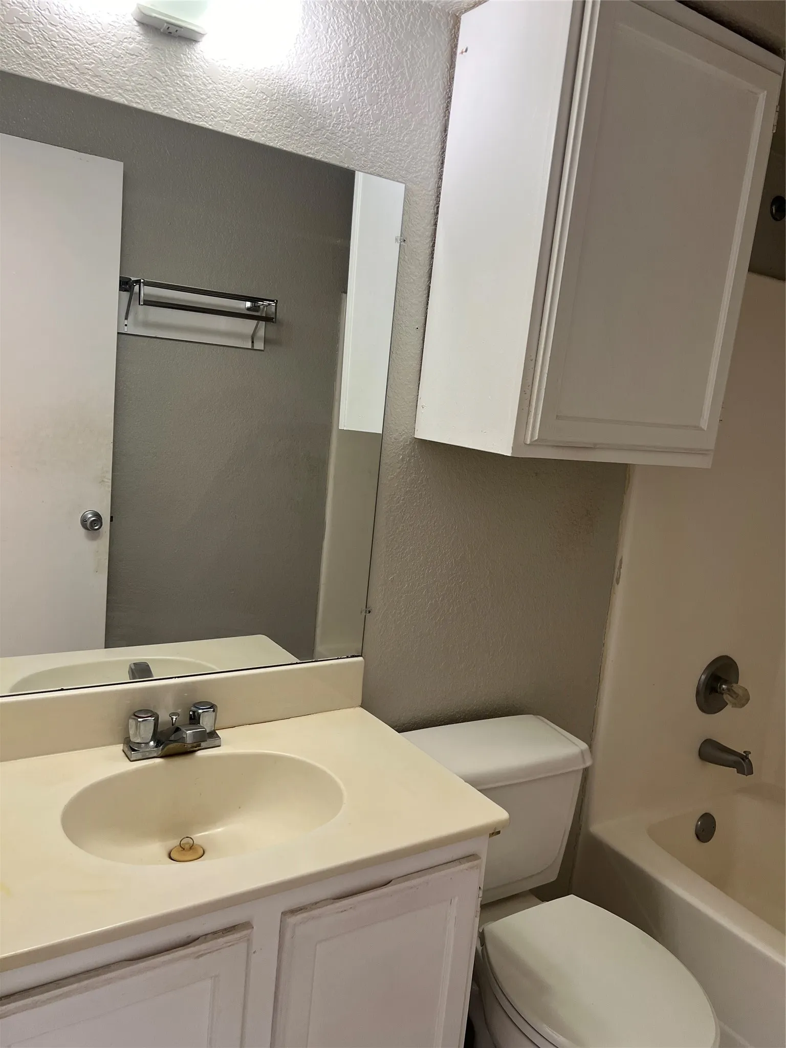 Vanity with integrated sink, wall-mounted mirror, white paneled cabinetry, and a full bathtub with shower